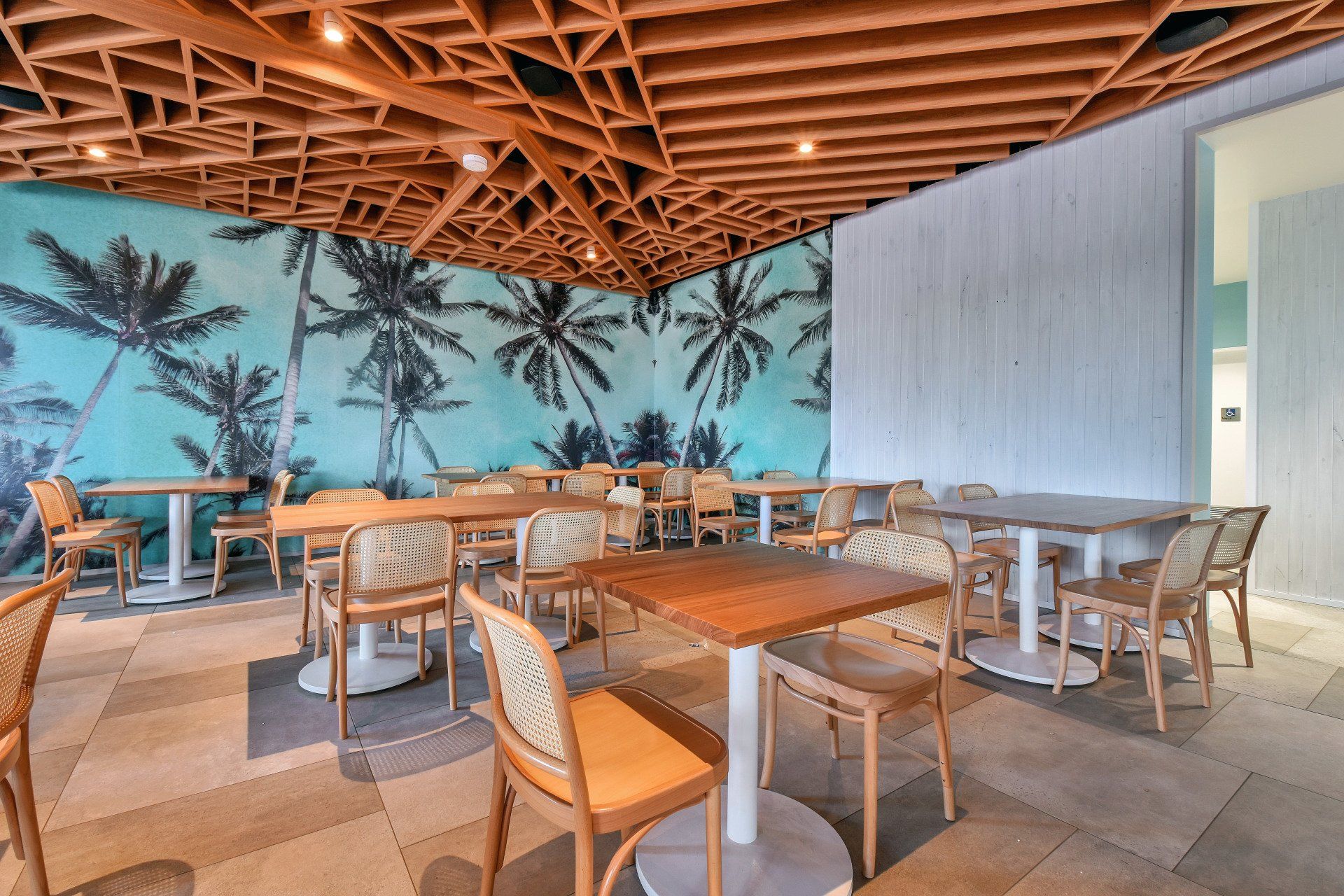 Restaurant interior with tables, chairs, palm tree mural, and a wood ceiling.