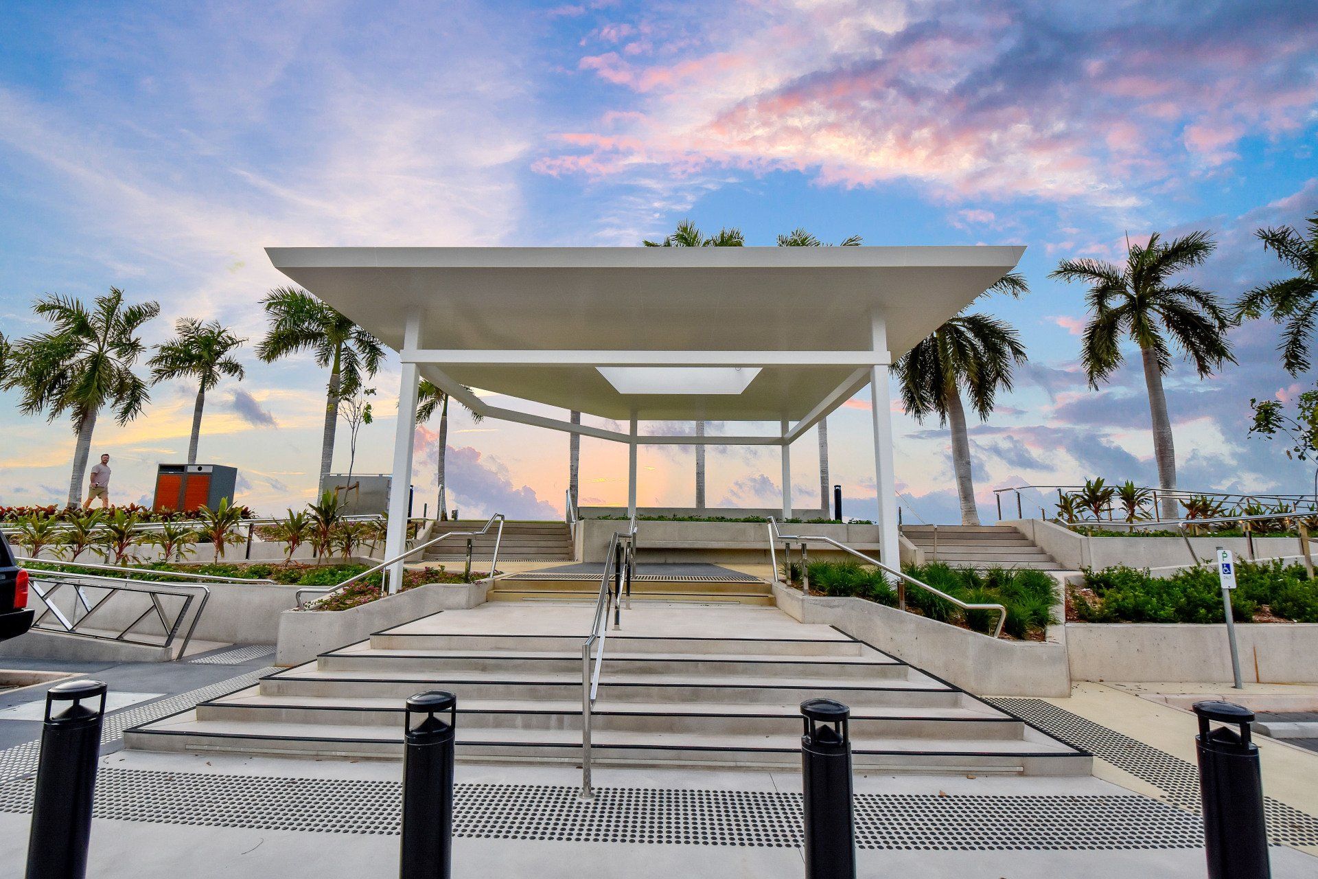 White pavilion with stairs, palm trees, and a cloudy sky.