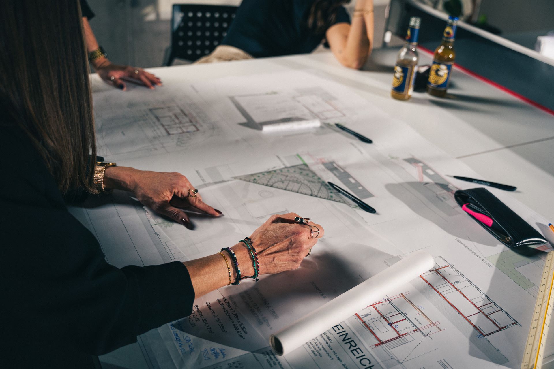 People reviewing architectural drawings on a table with bottles and pens nearby