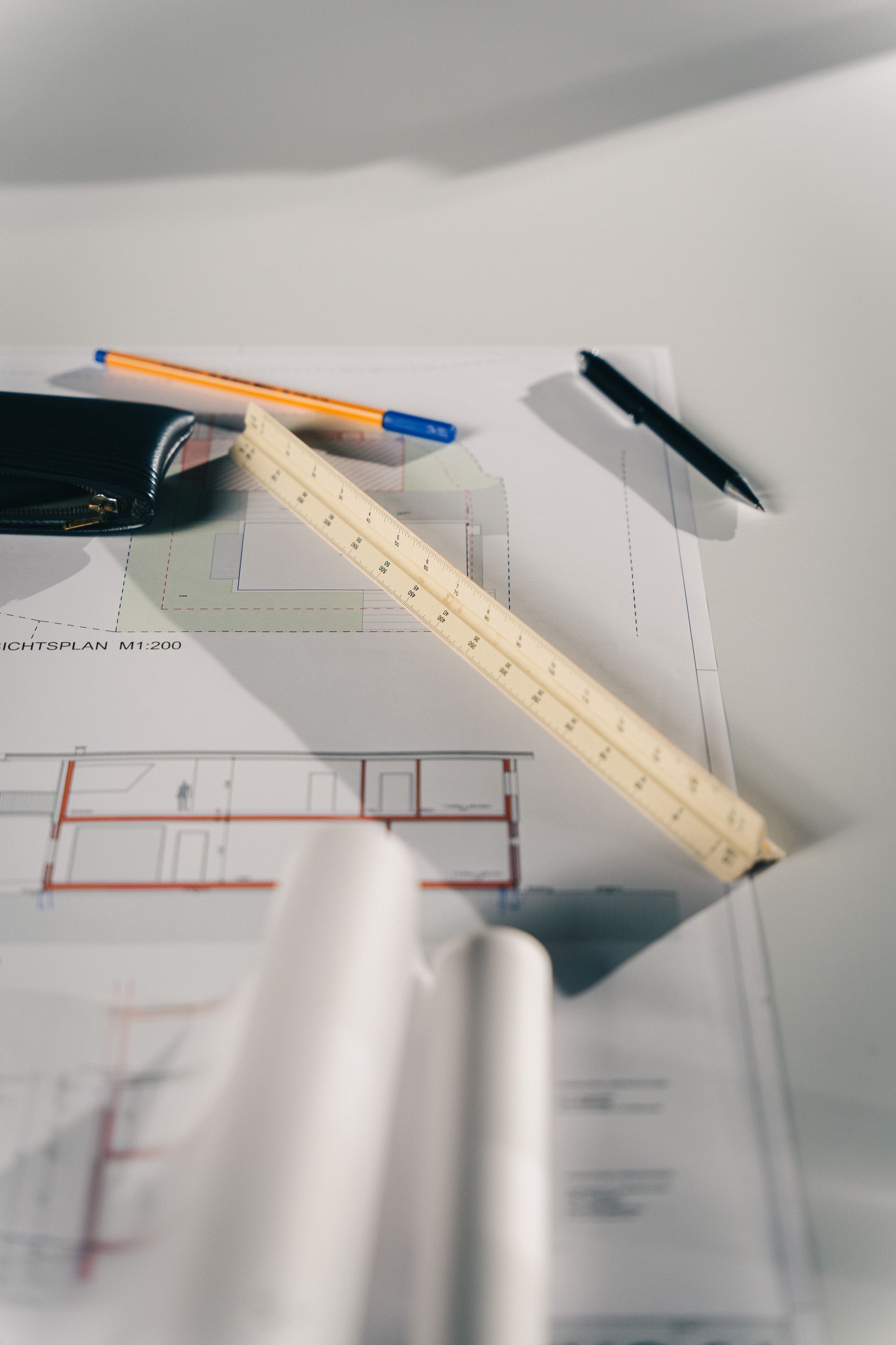 Desk with pencils, ruler, pen, eyeglasses, and papers with sketches and text under soft light