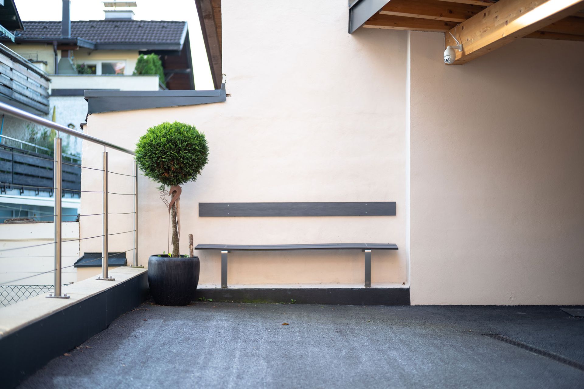 Small courtyard with a bench, potted topiary tree, and staircase beside a beige wall.