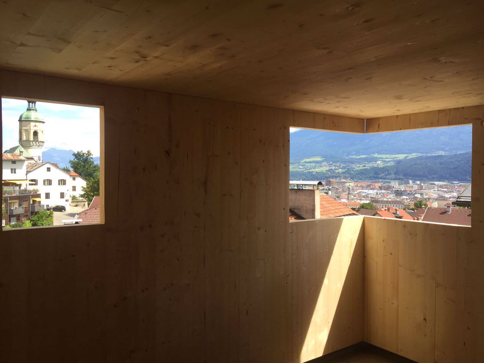 Wood-paneled room with two windows overlooking a town and mountains