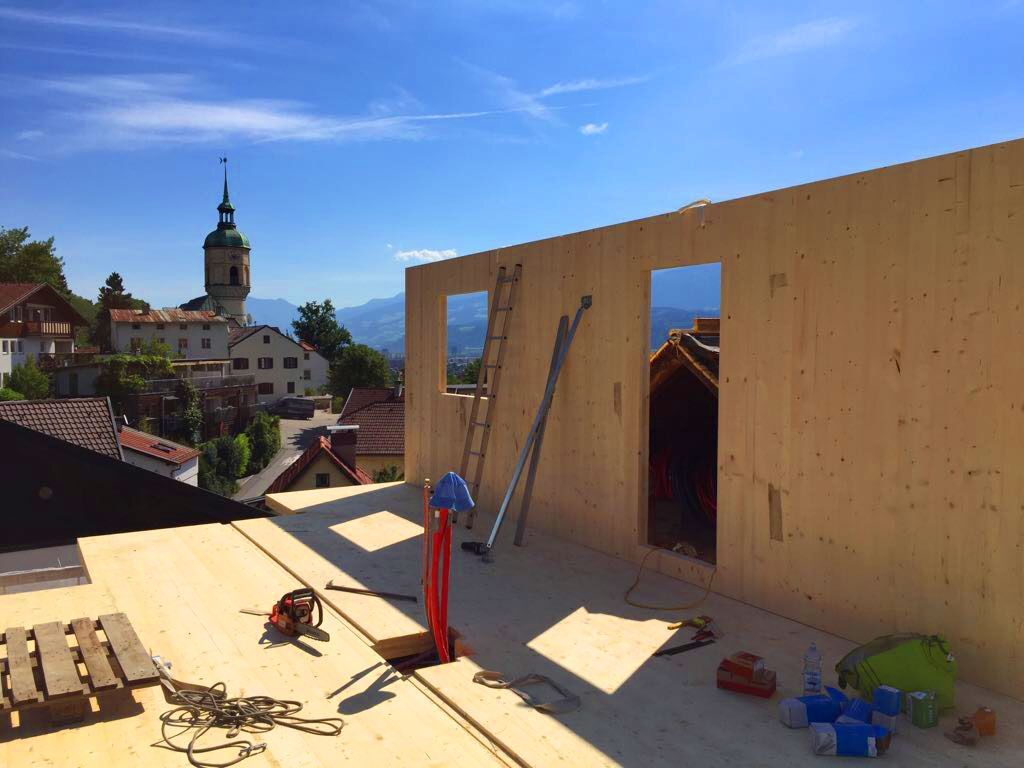 Rooftop construction site with wooden walls, ladders, tools, and a town church in the background