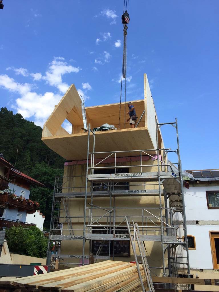 Scaffolding around a building under construction with workers installing a wooden roof frame under a blue sky