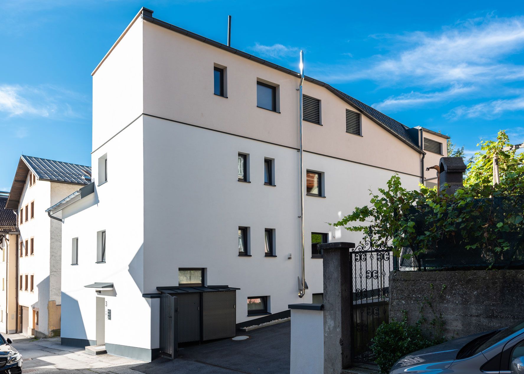 White multi-story residential building with balconies and a gated entrance on a sunny street