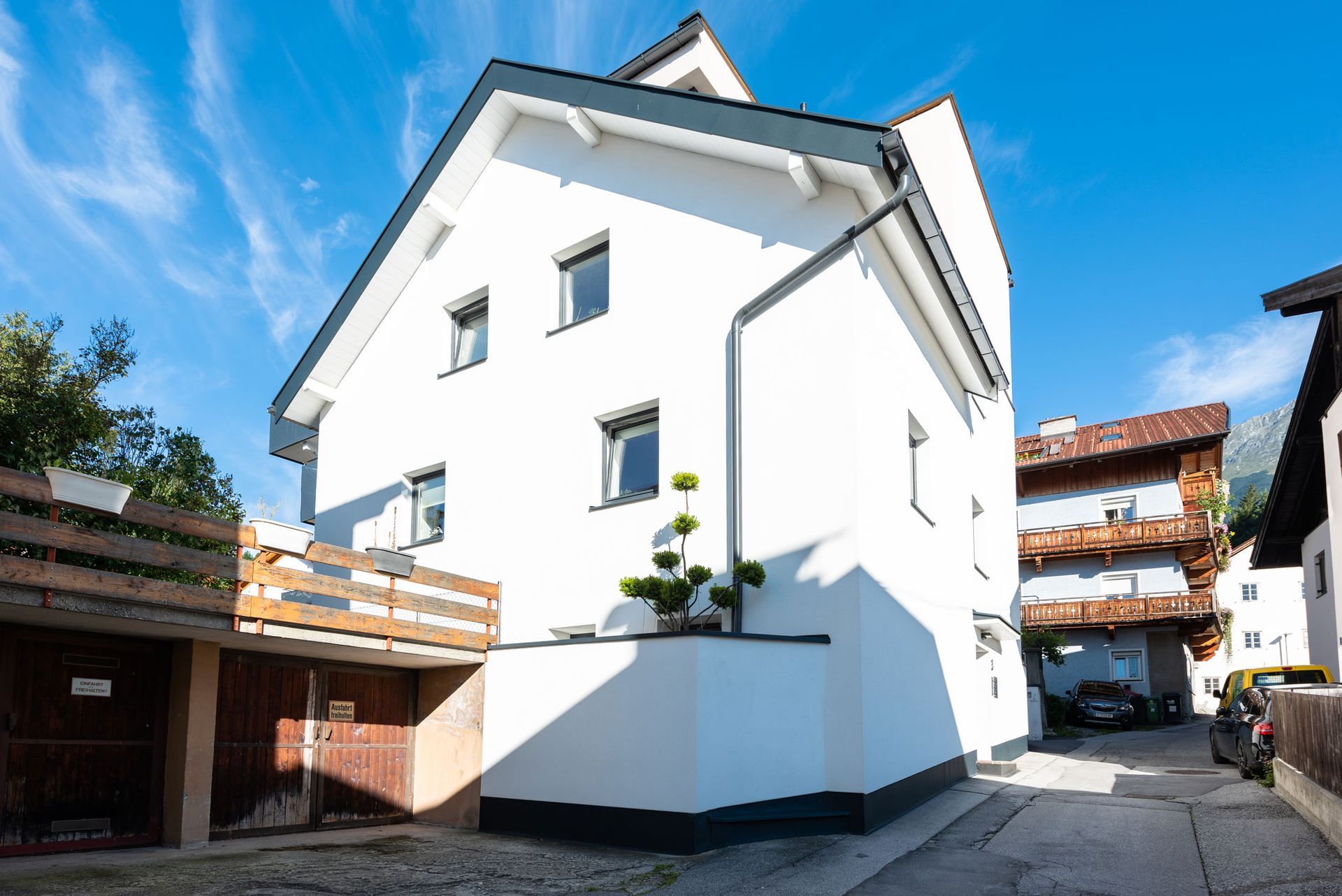 White house with a sloped roof and balconies on a sunny street under a clear blue sky