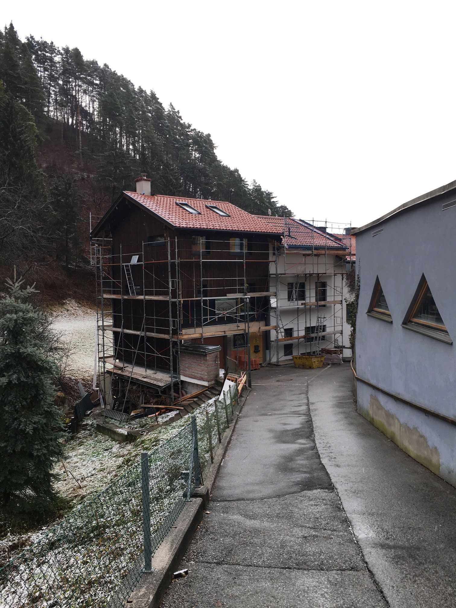 Narrow snowy lane beside old buildings on a hillside, with scaffolding on one house.
