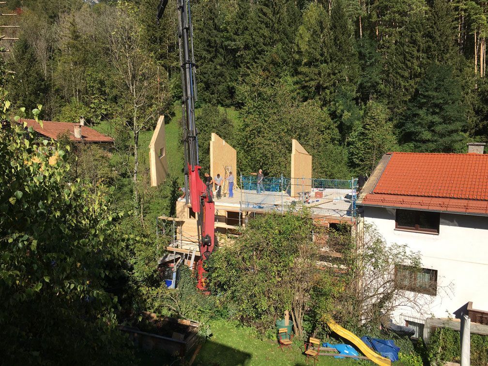 Backyard construction site with a red crane, partially built walls, and a white house beside trees