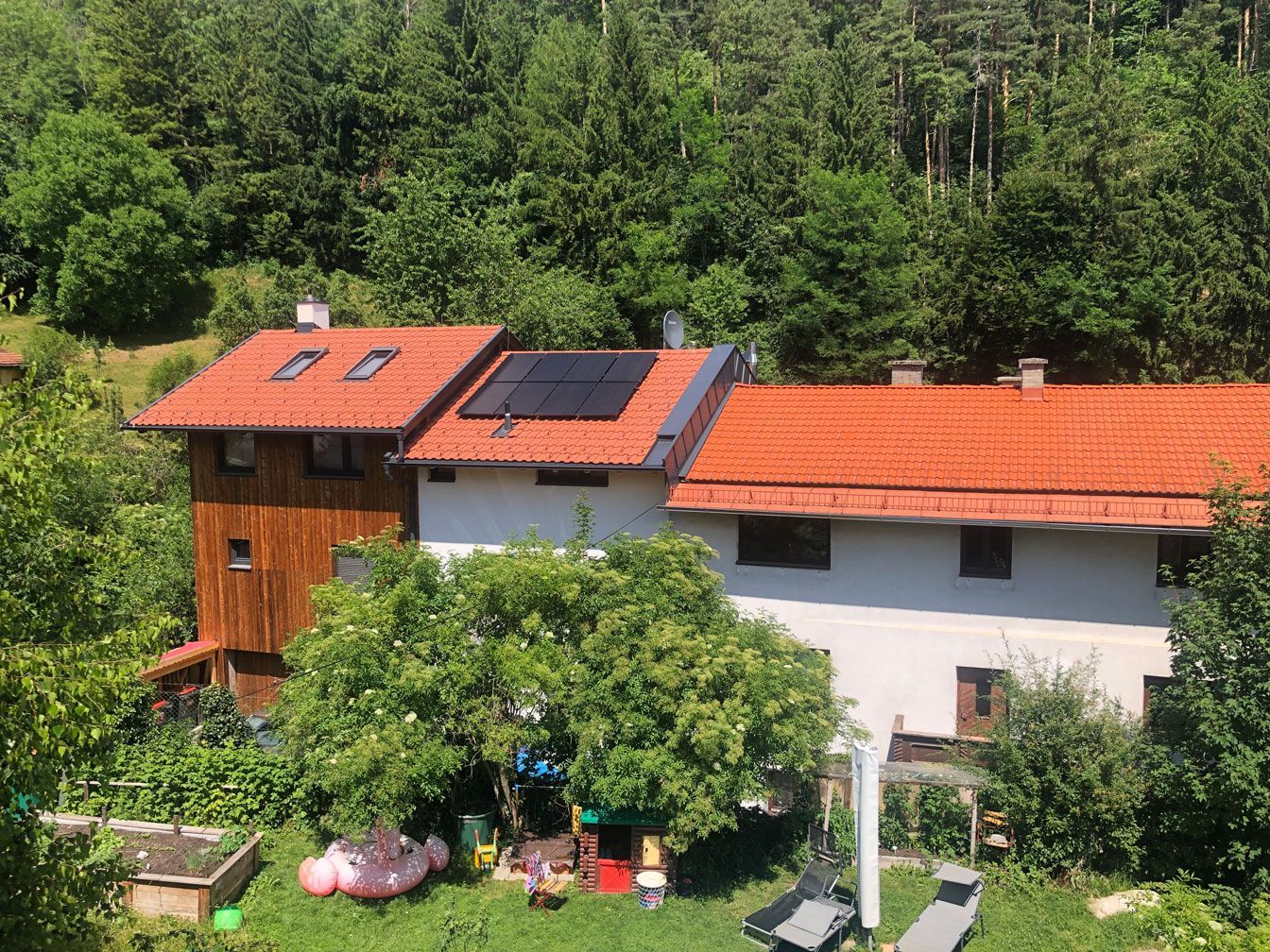 Countryside house with red roof and solar panels, surrounded by lush green trees and garden.