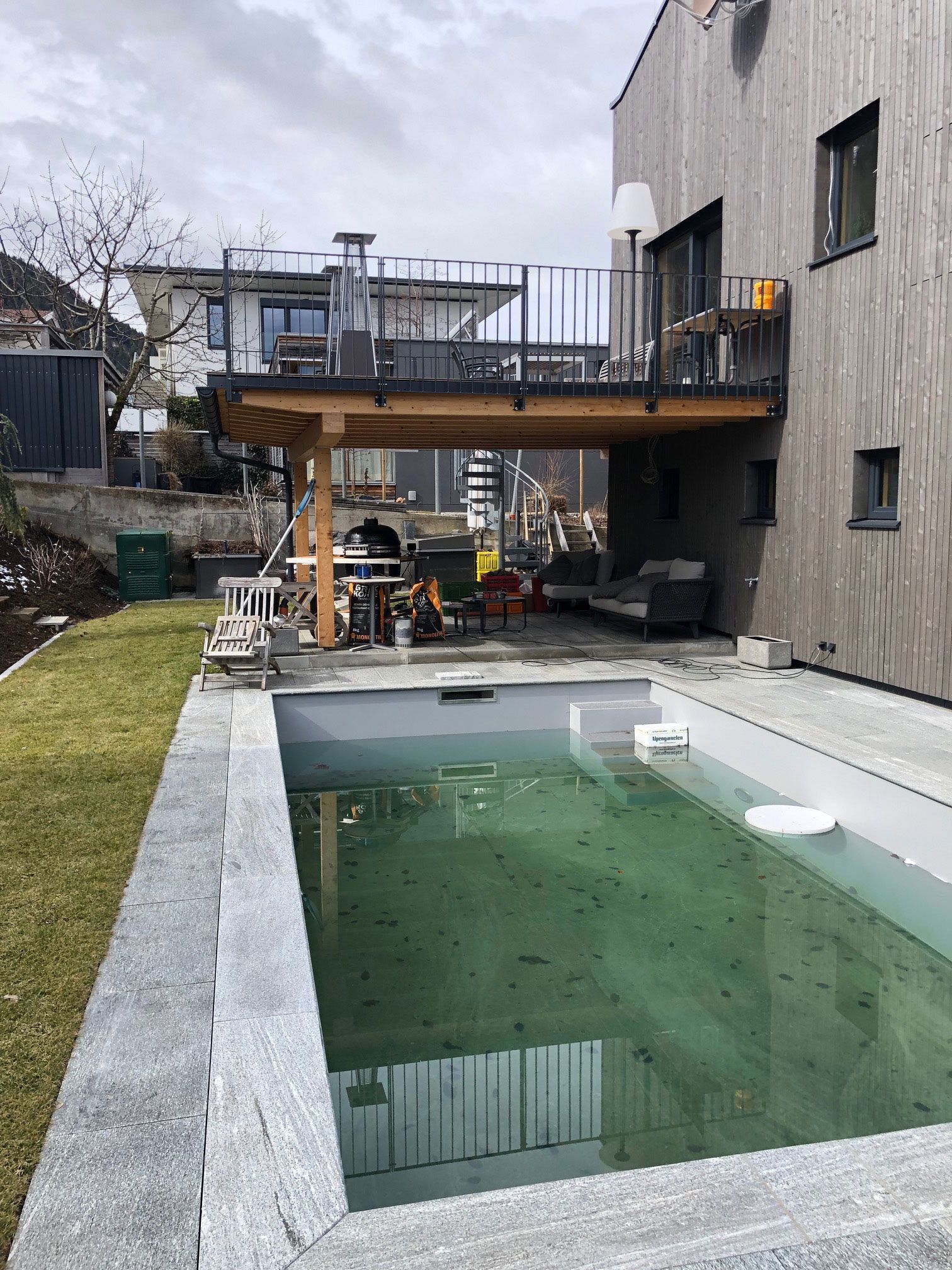 Backyard with a small rectangular pool beside a gray house and raised wooden deck