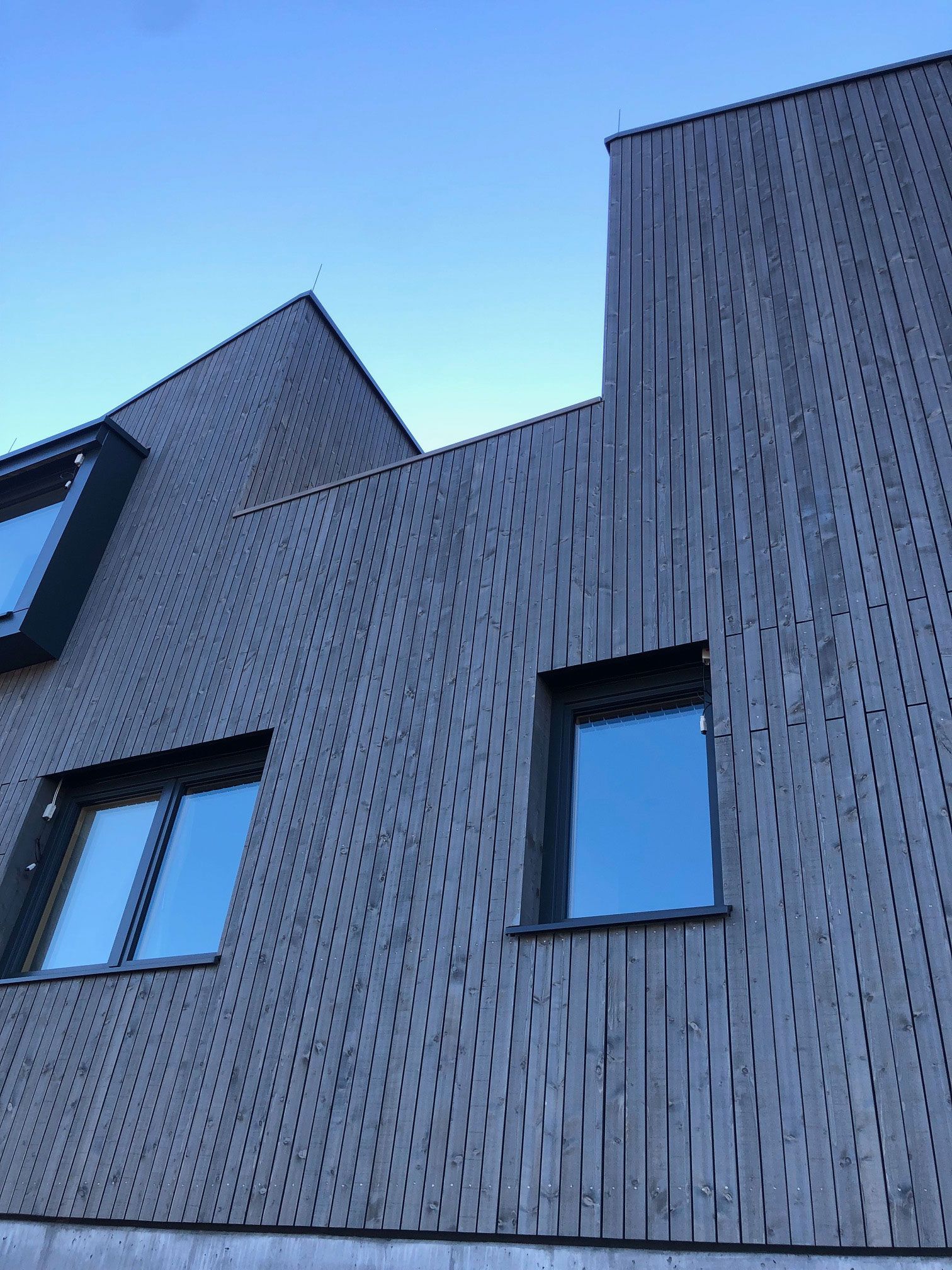 Modern gray building facade with textured panels and angular rooflines against a blue sky