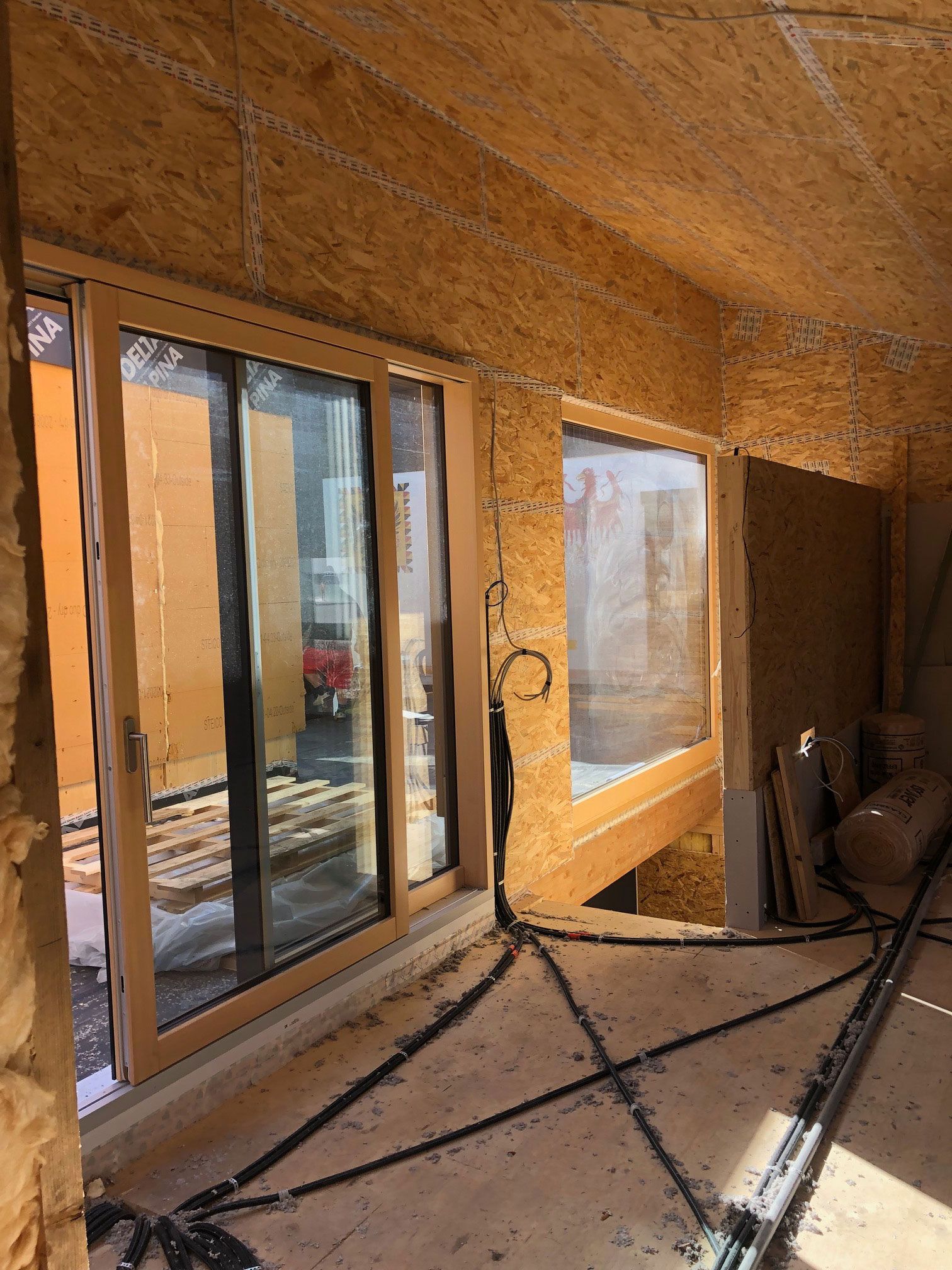 Sunlit unfinished room with large windows, exposed insulation, and construction materials on the floor