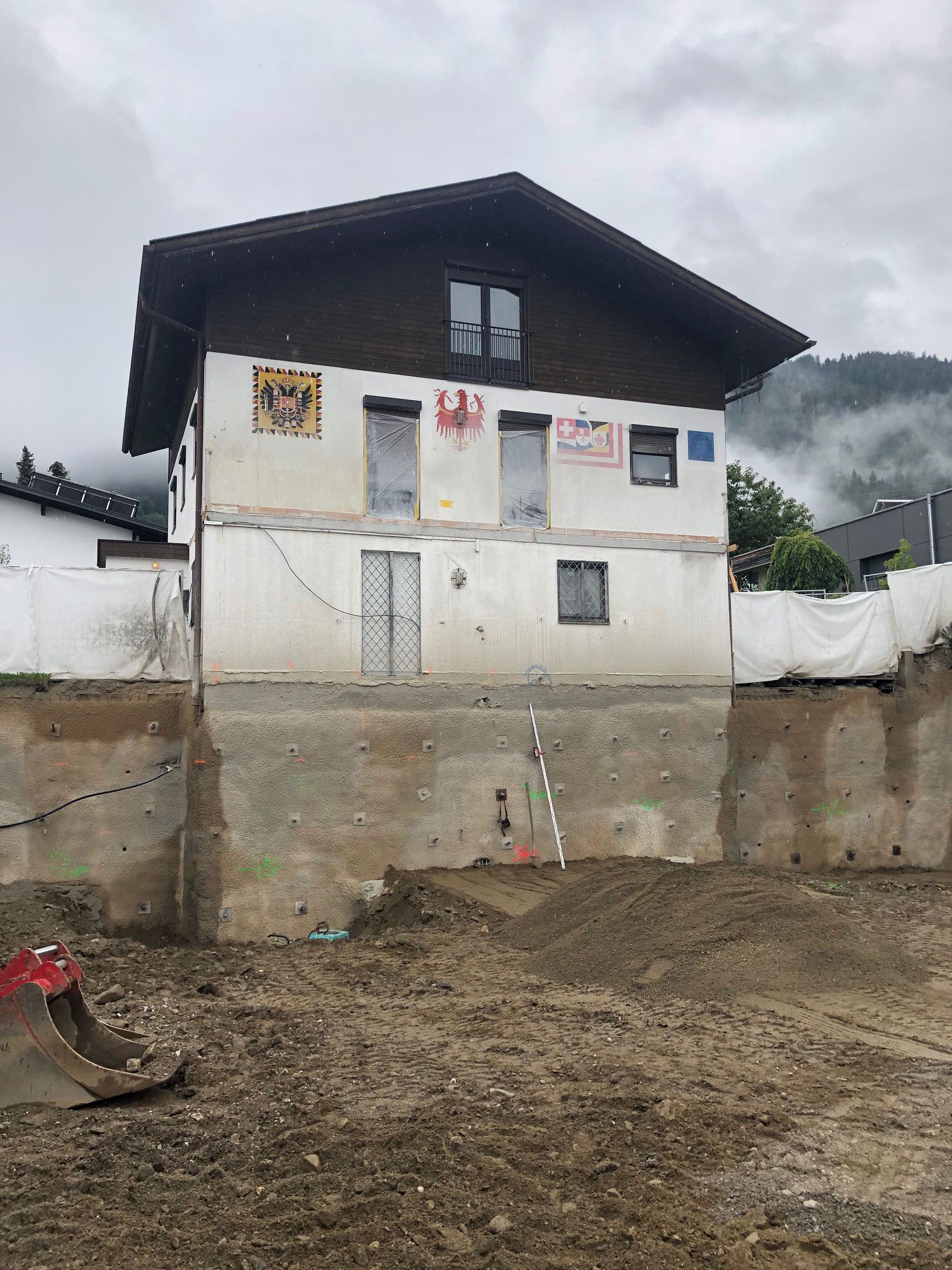 Partially constructed house with white walls and a dark roof on a muddy, excavated lot