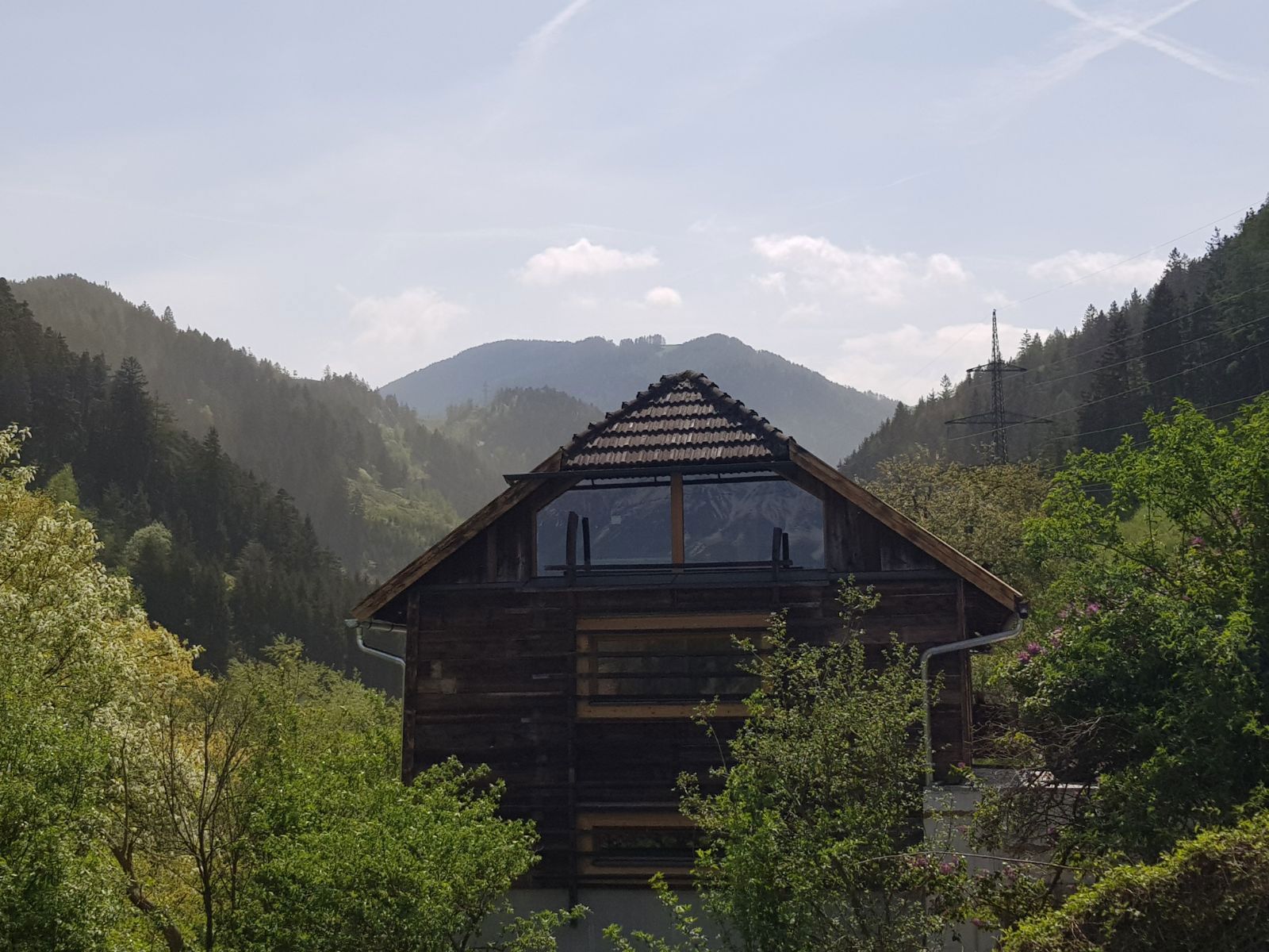 Wooden cabin nestled in a green mountain valley under a pale sky