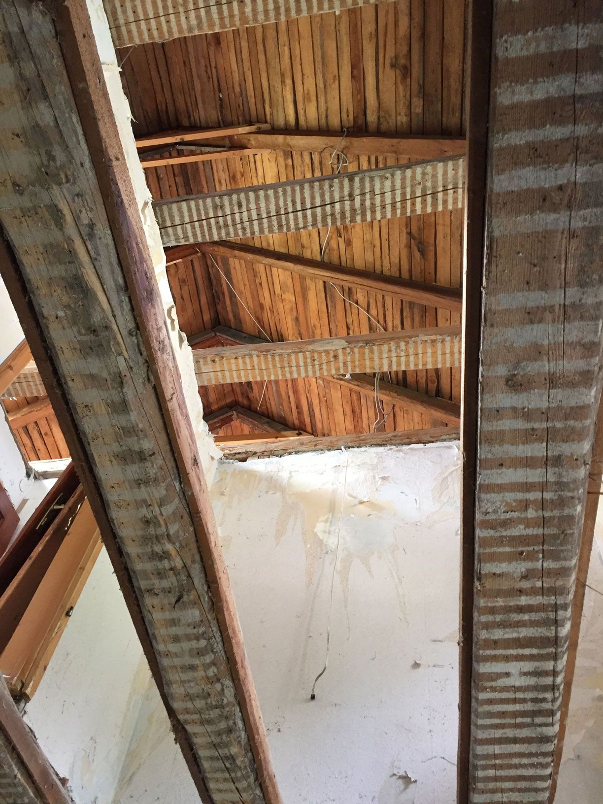 View of an exposed wooden roof and beams above a white wall, showing a skylight opening.