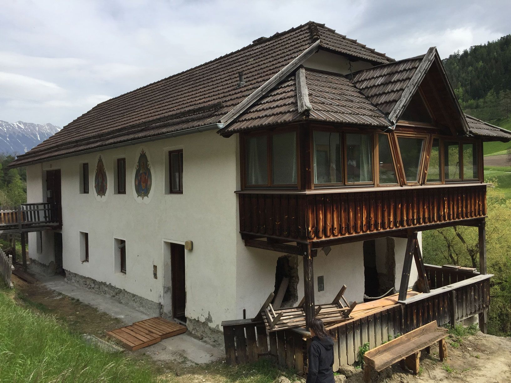 Old white house with a dark tiled roof and wooden balcony on a grassy hillside