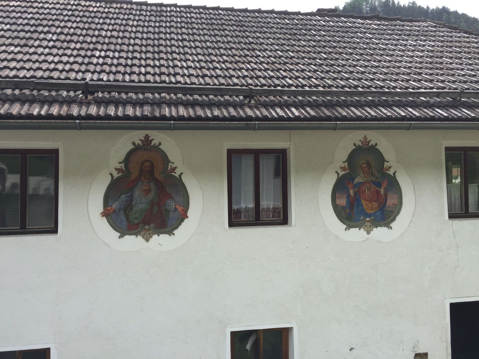 White house wall with two religious murals beneath a tiled roof and small windows.