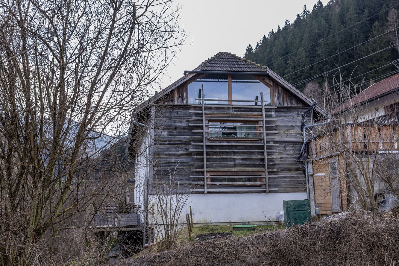 Weathered wooden barn on a hillside, surrounded by bare trees and brush.