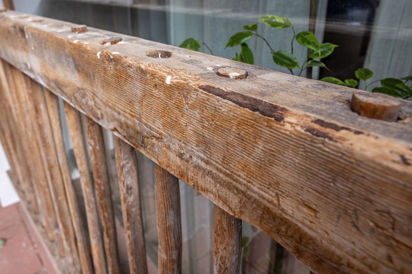 Close-up of a weathered wooden railing with peeling paint and visible rusted bolts.