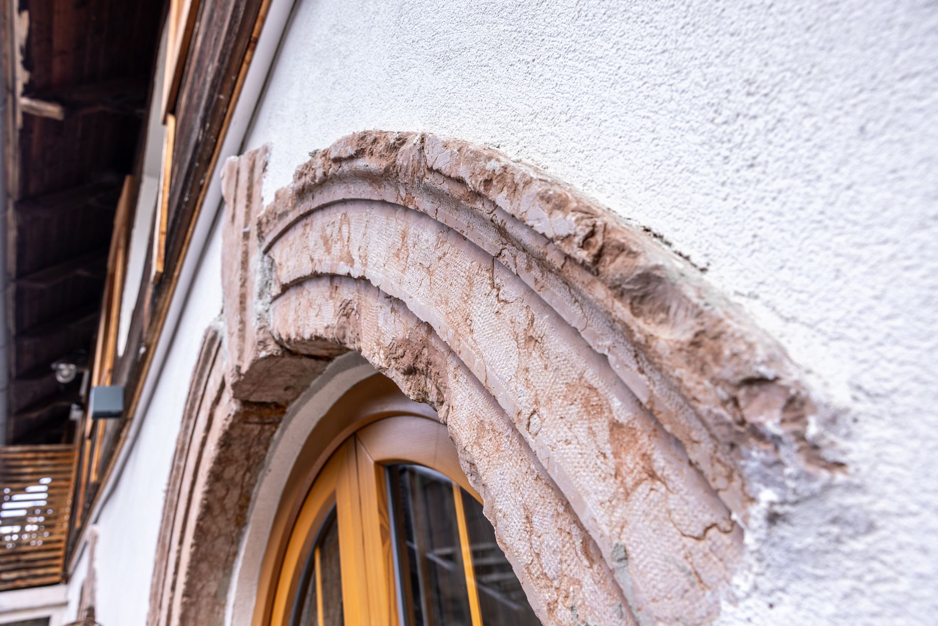 Close-up of a weathered stone arch above a window on a white stucco building