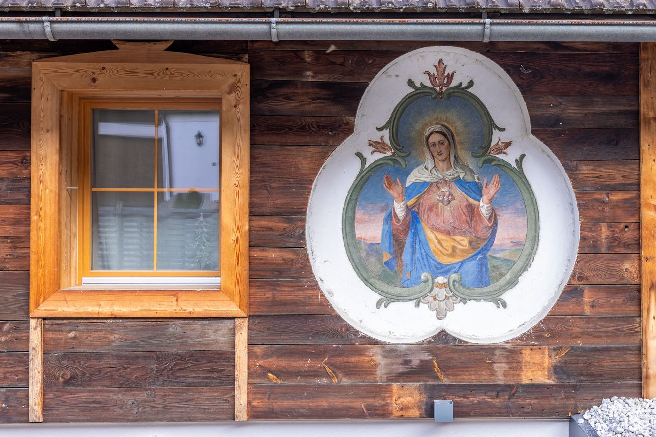 Wooden cabin wall with a window and a painted religious mural in an ornate white frame