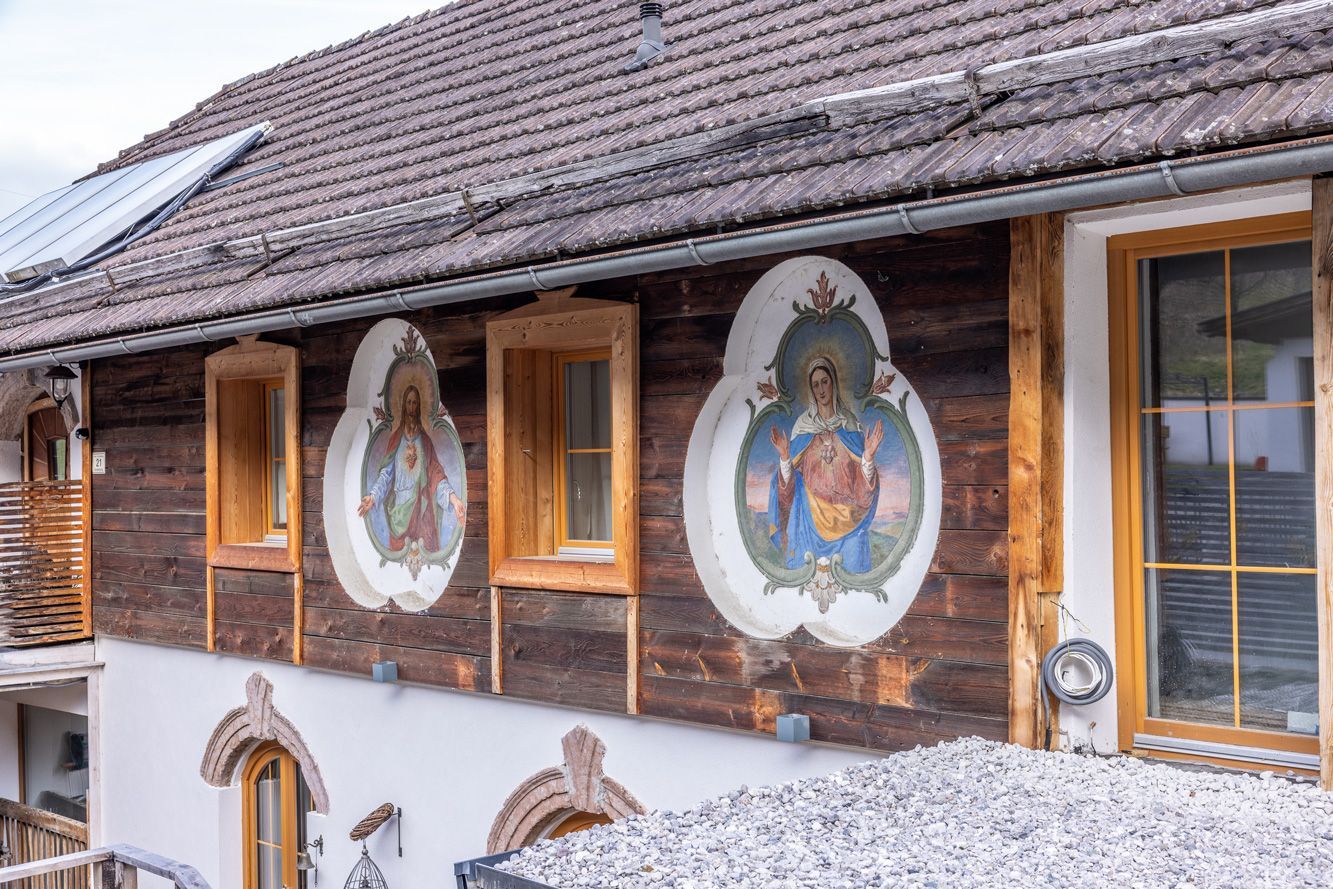 Rustic chalet exterior with painted religious murals on wooden walls and a snow-covered roof