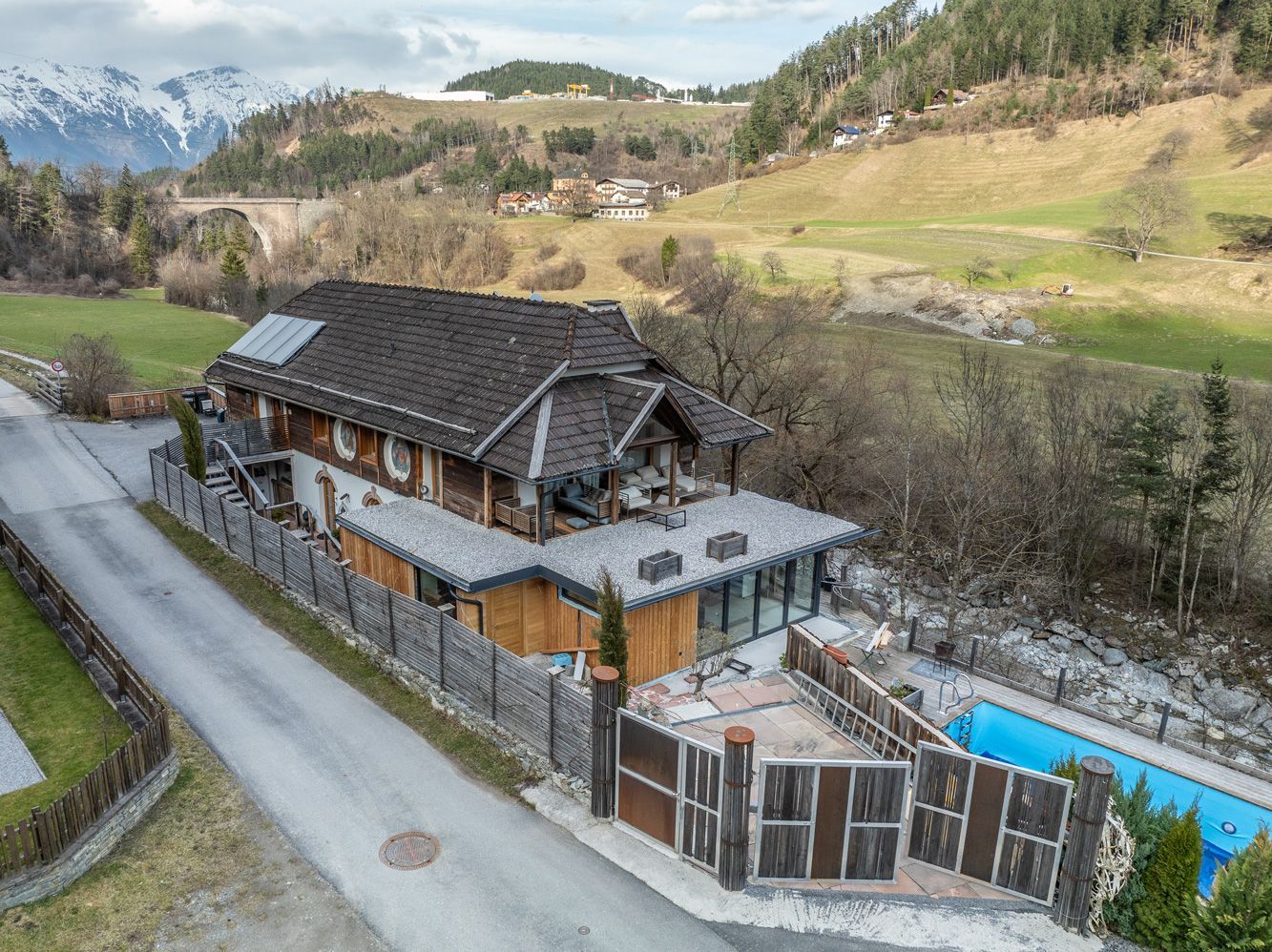 Aerial view of a rustic house with a fenced yard and blue swimming pool in a rural valley