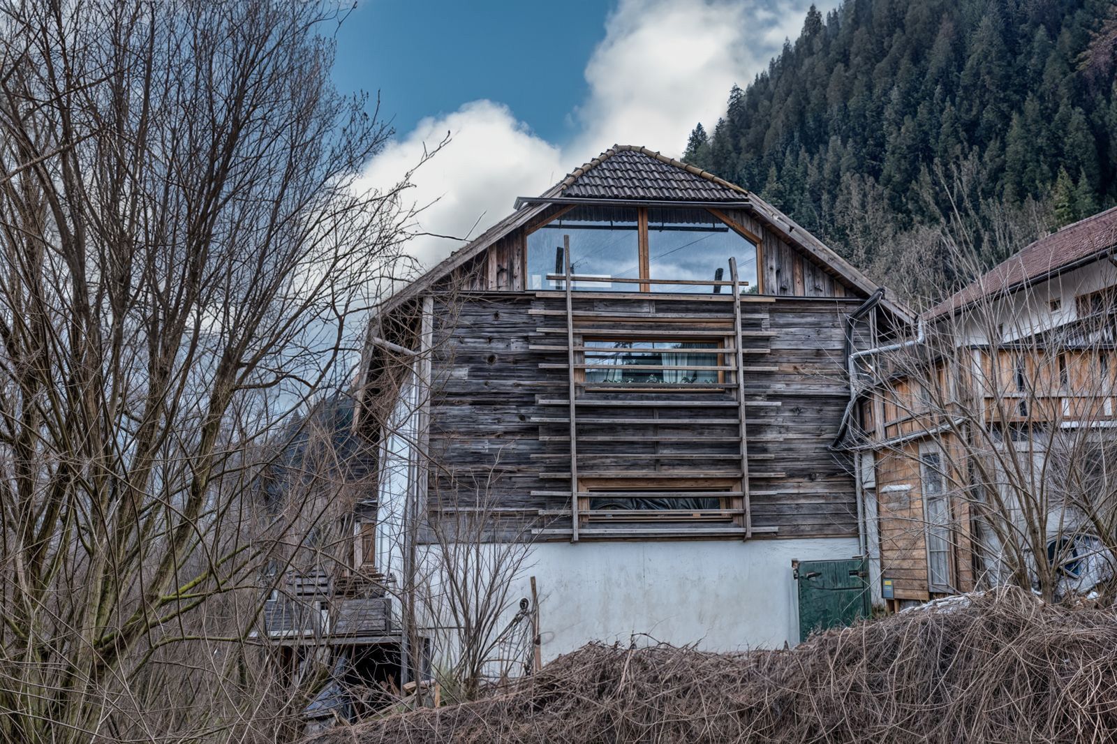 Weathered wooden barn in a winter landscape with bare trees and mountains in the background