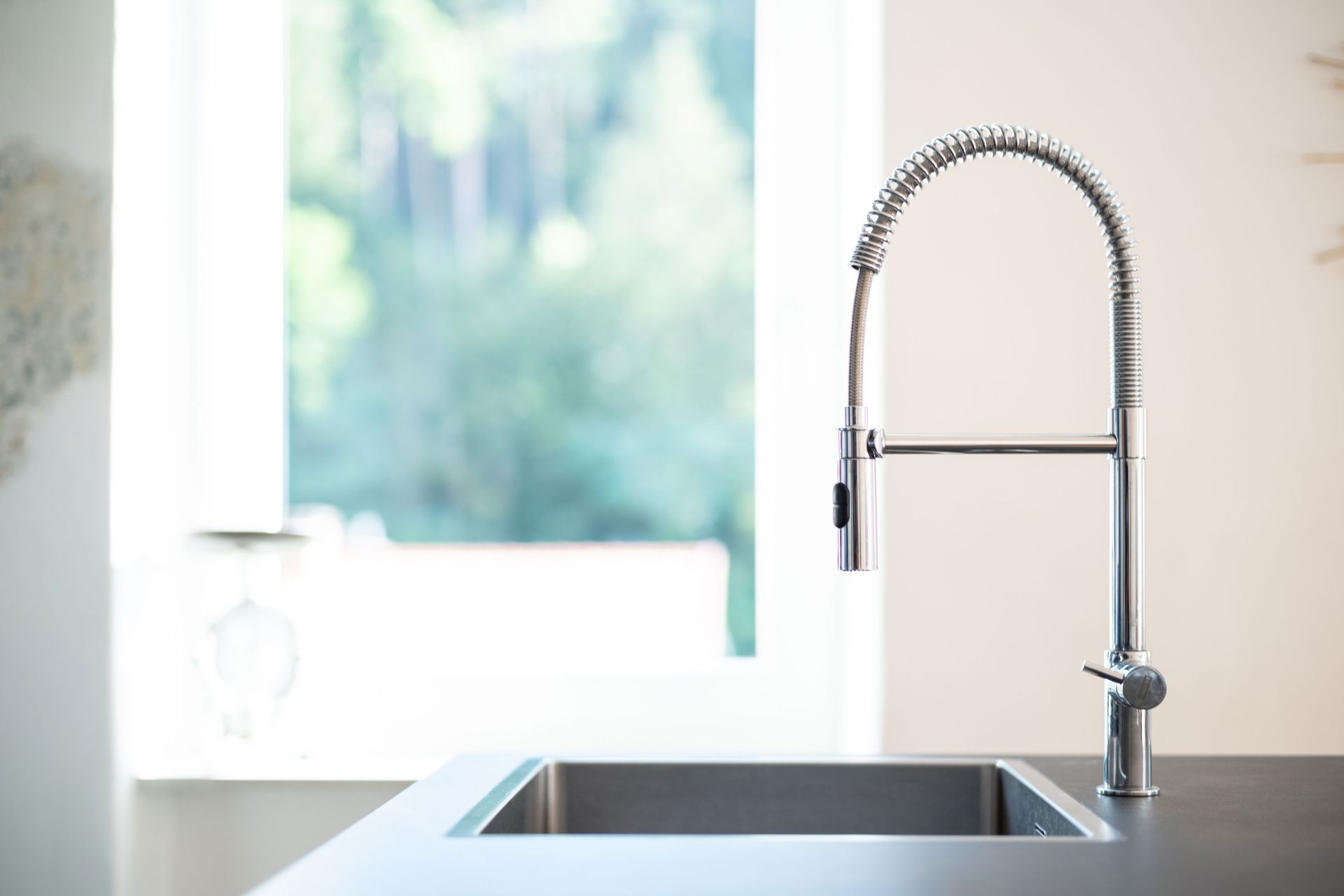 Modern kitchen sink with tall spring faucet by a bright window