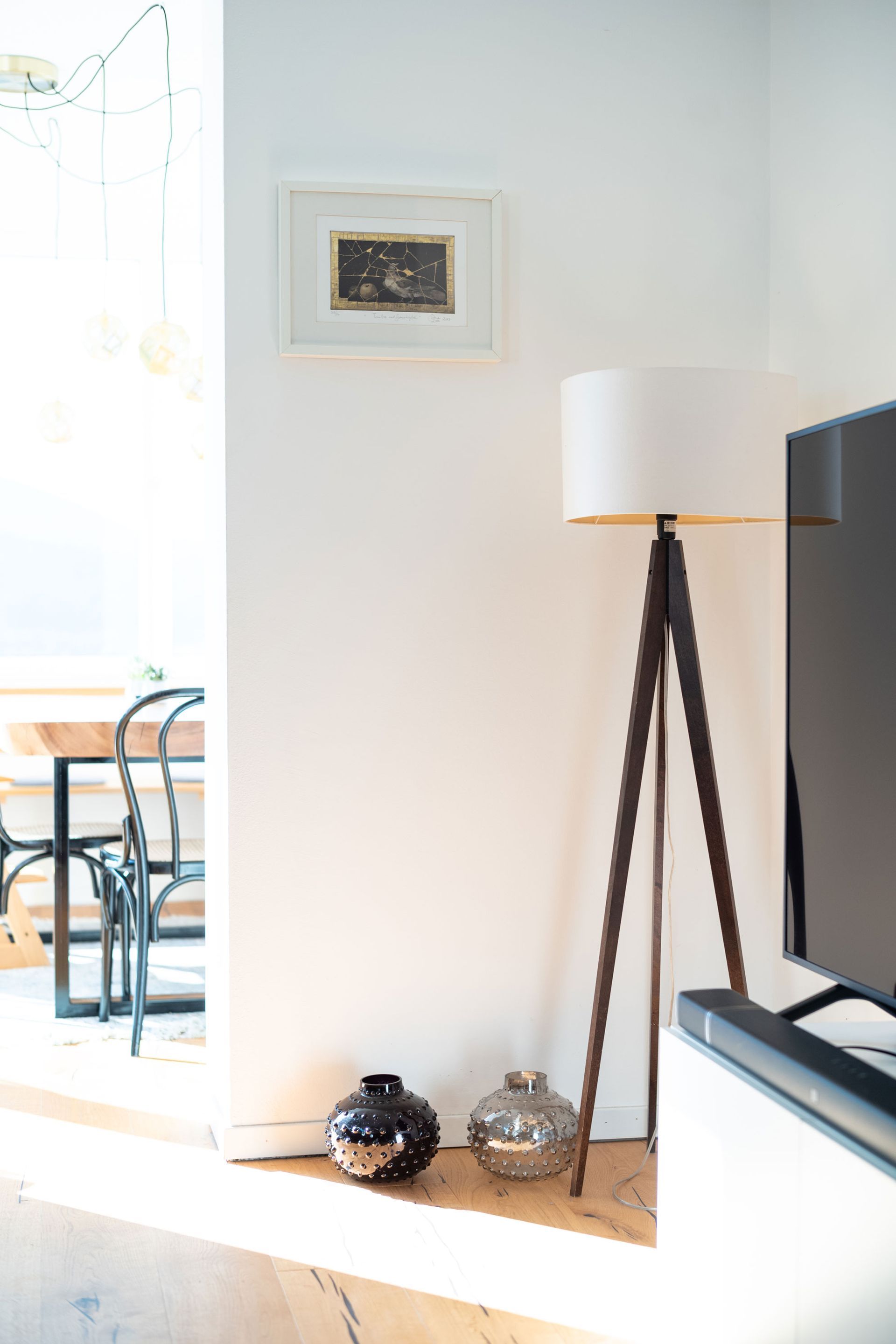 Bright living room corner with tripod floor lamp, wall art, and TV beside a sunlit patio door