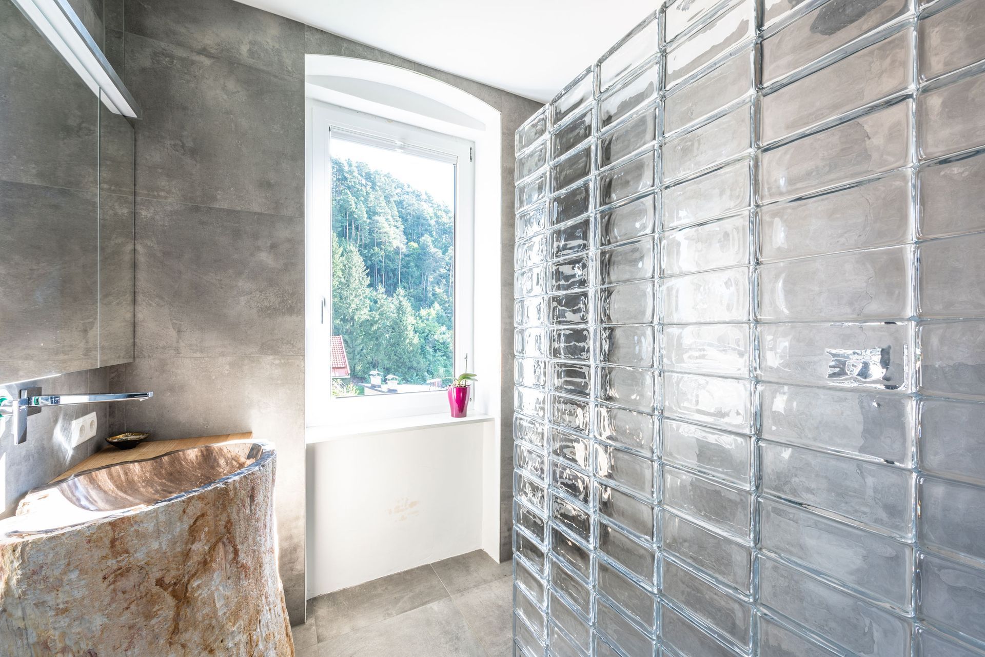 Modern bathroom with stone sink, gray tiled walls, and a bright window with trees outside