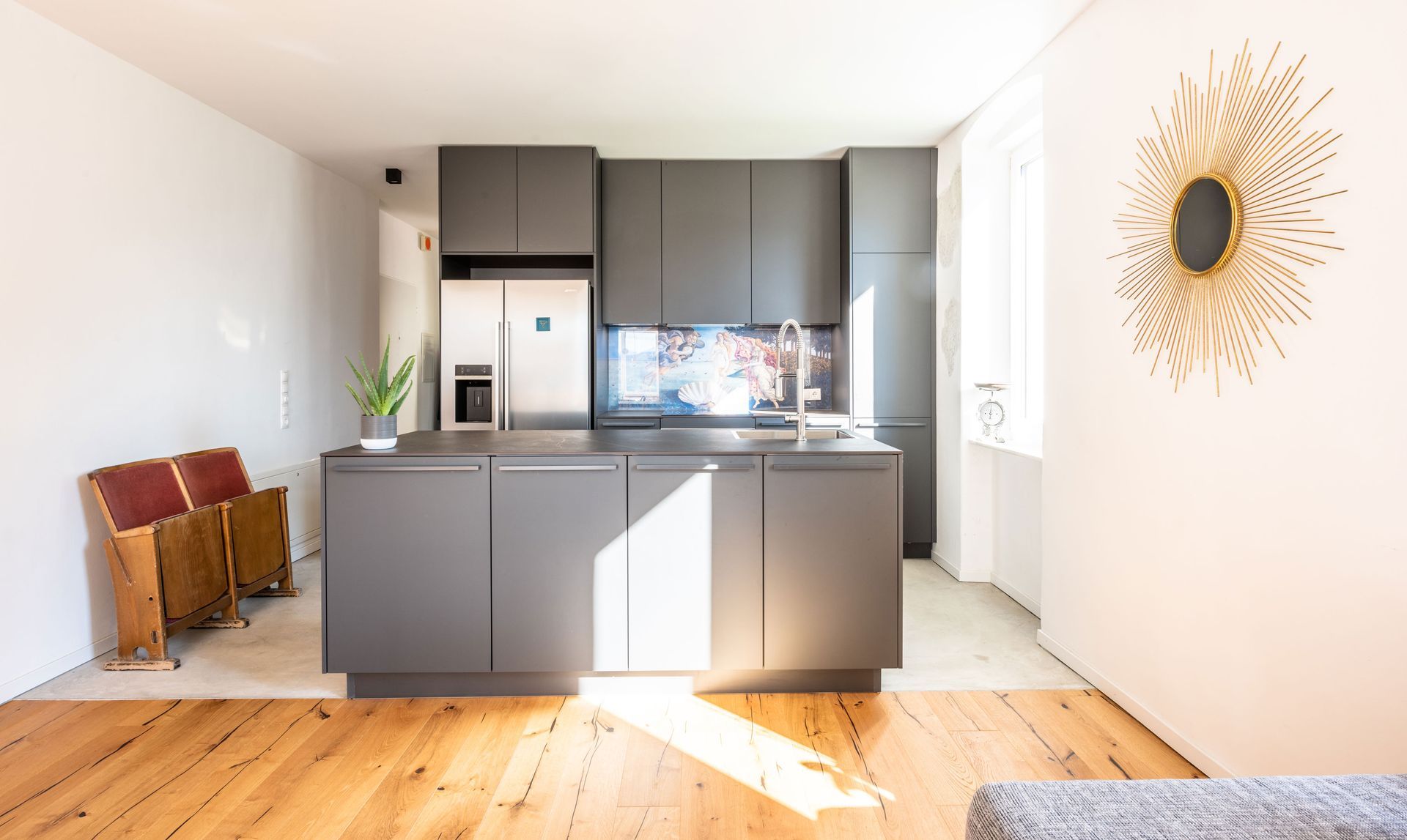 Bright modern kitchen with gray cabinets, white walls, and wood floors in a sunlit room.