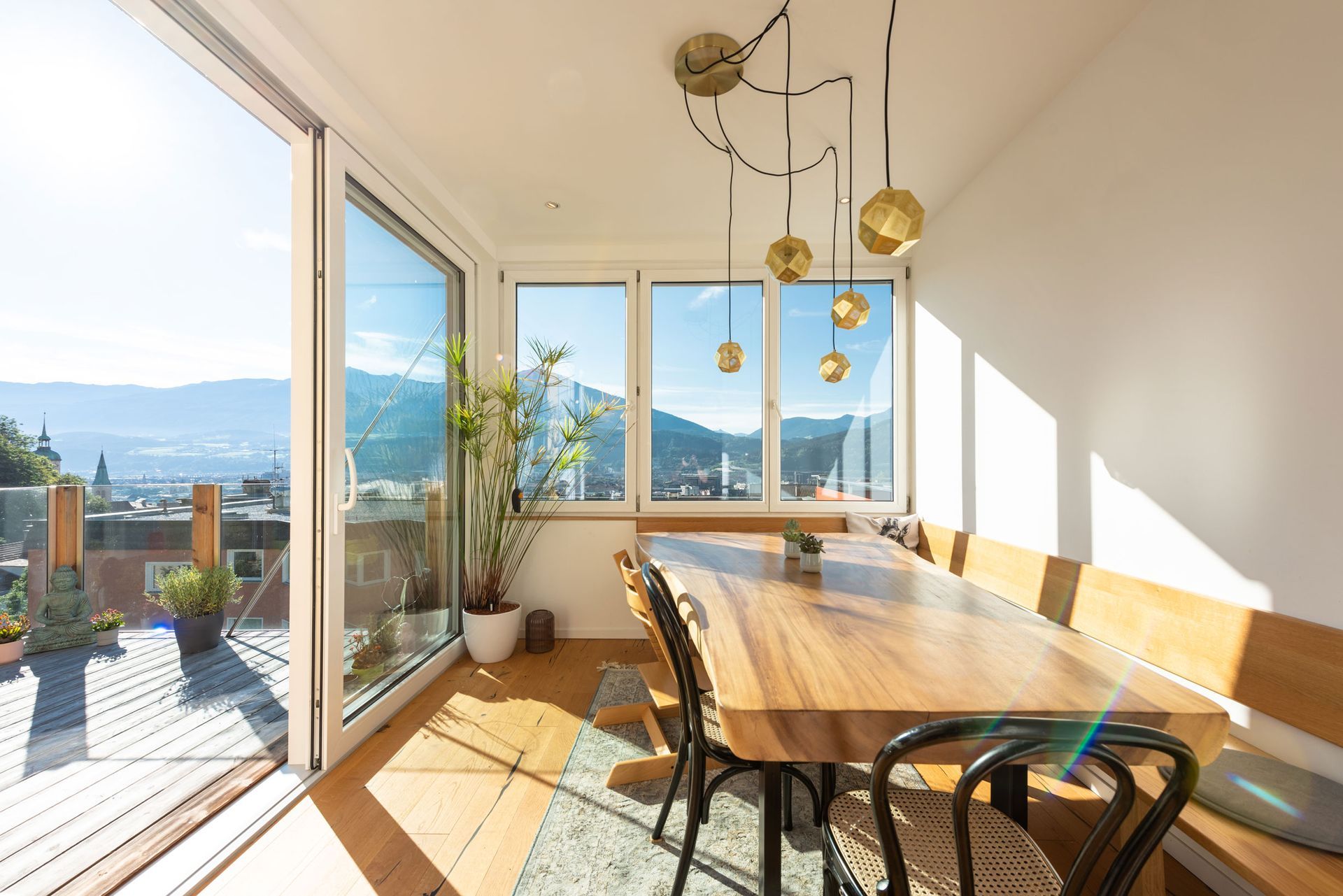 Bright dining room with wooden table, chairs, large windows, and a sunlit mountain view.