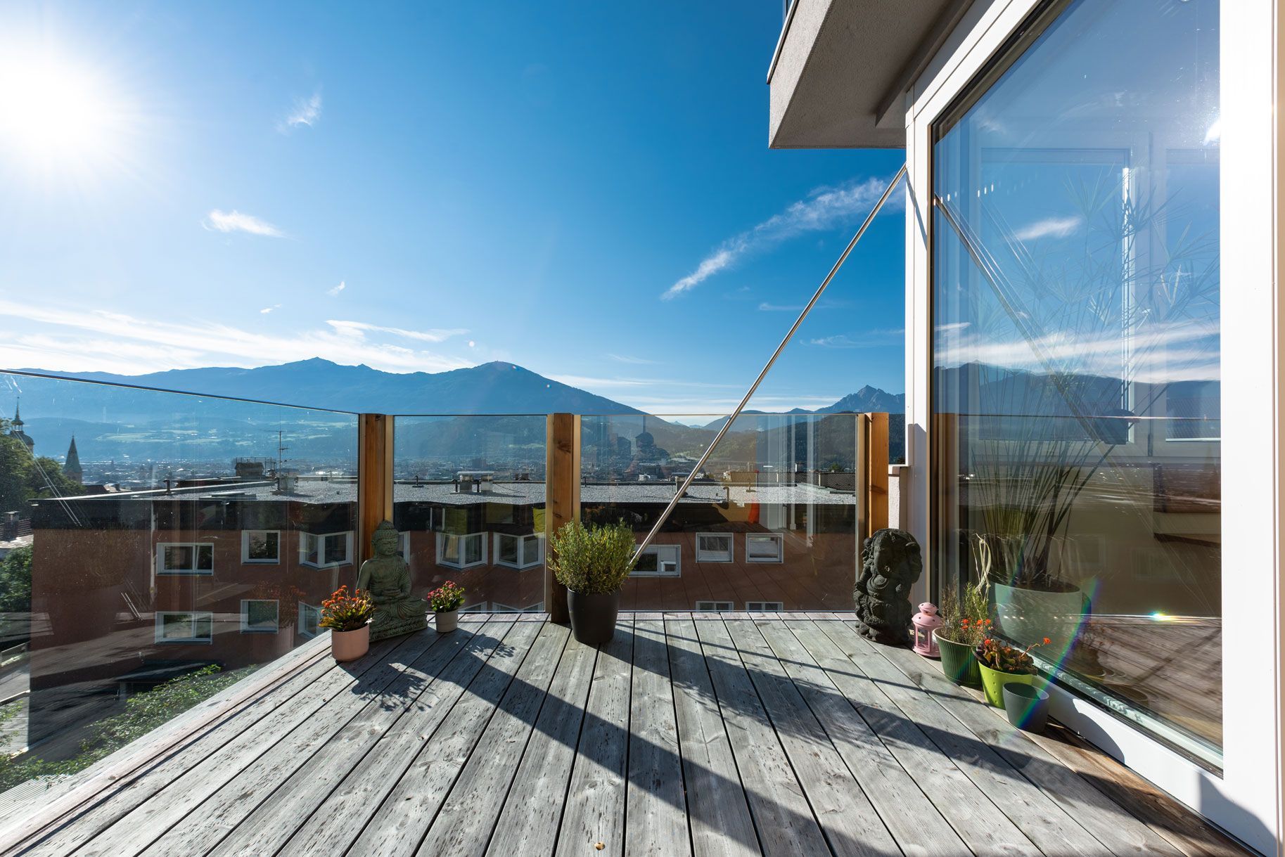 Sunny rooftop deck with potted plants, ocean view, and mountains in the distance