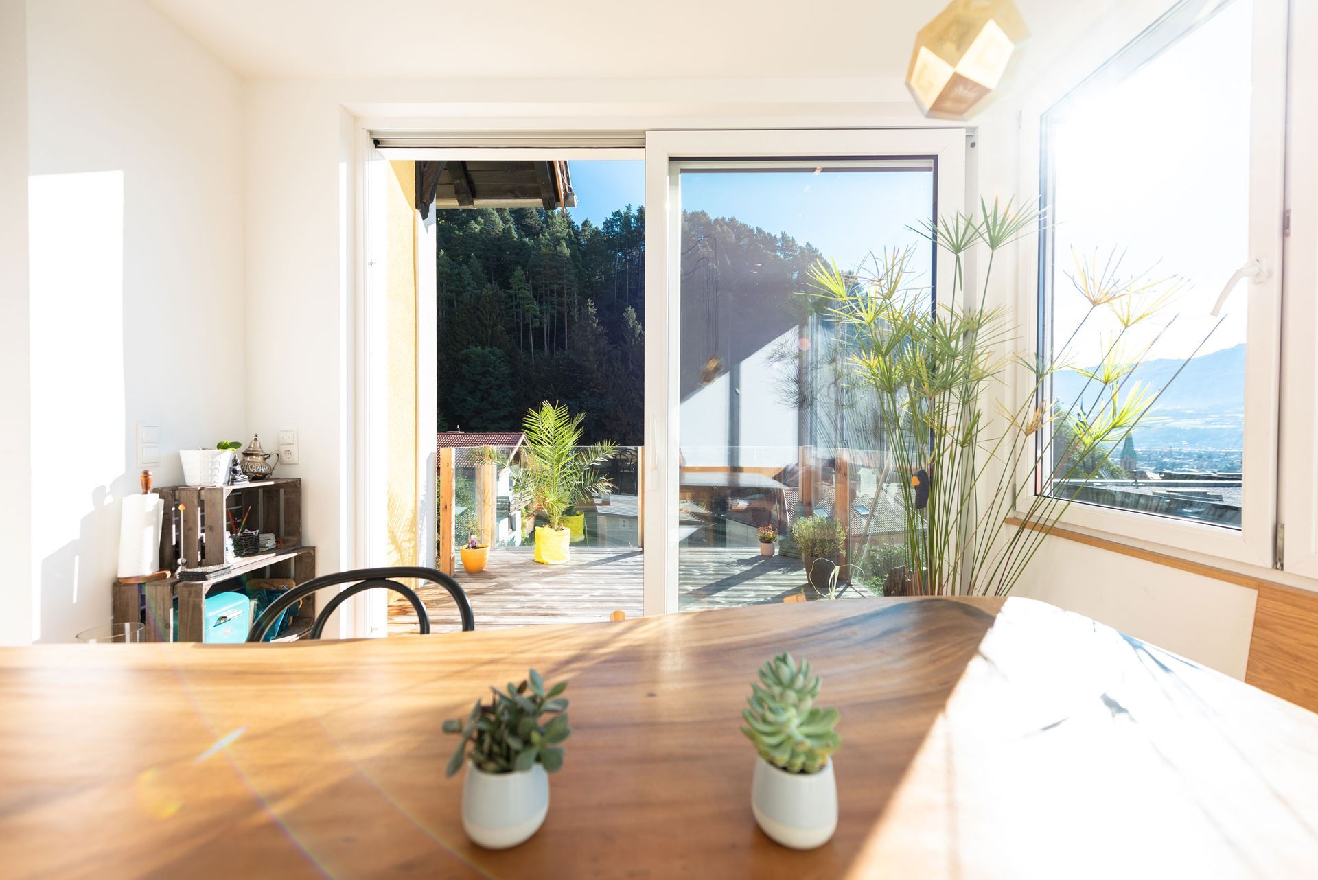 Bright dining room with wooden table, small plants, and large sliding doors opening to a sunny patio and sea view
