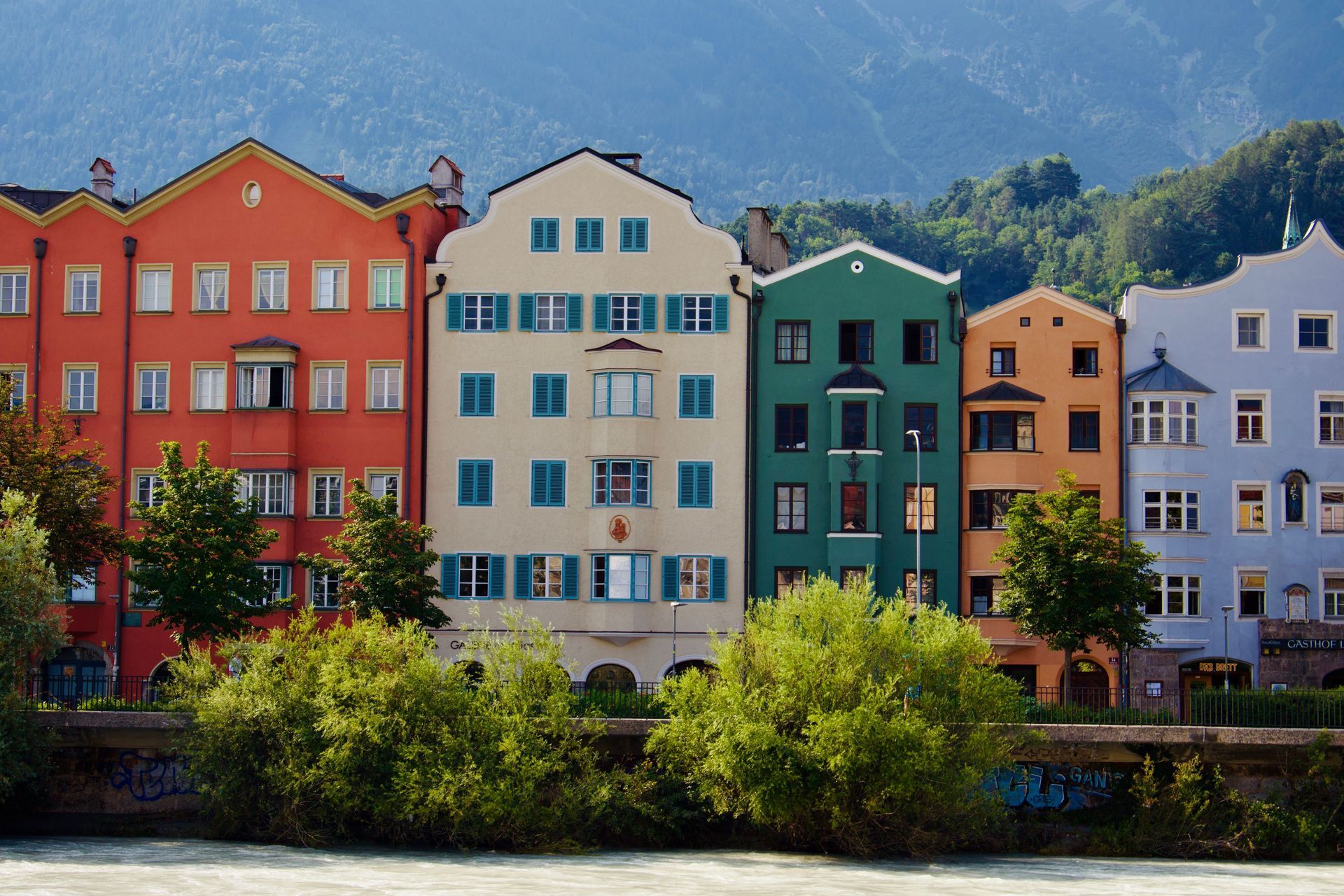 Colorful riverside row of buildings with trees and mountains in the background