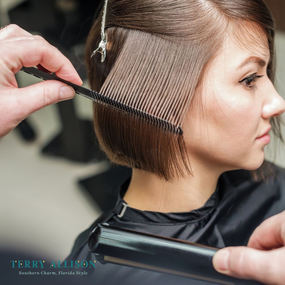 Woman getting her hair cut in a salon; stylist combing and holding a flat iron.
