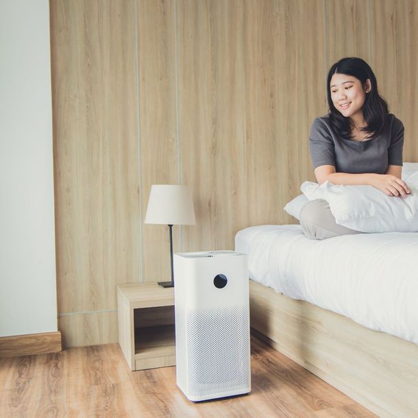 a woman is sitting on a bed next to a air purifier .