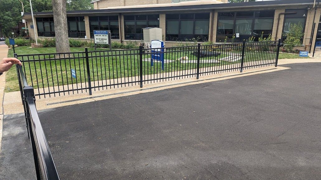 A person is spraying water on a fence in front of a building.