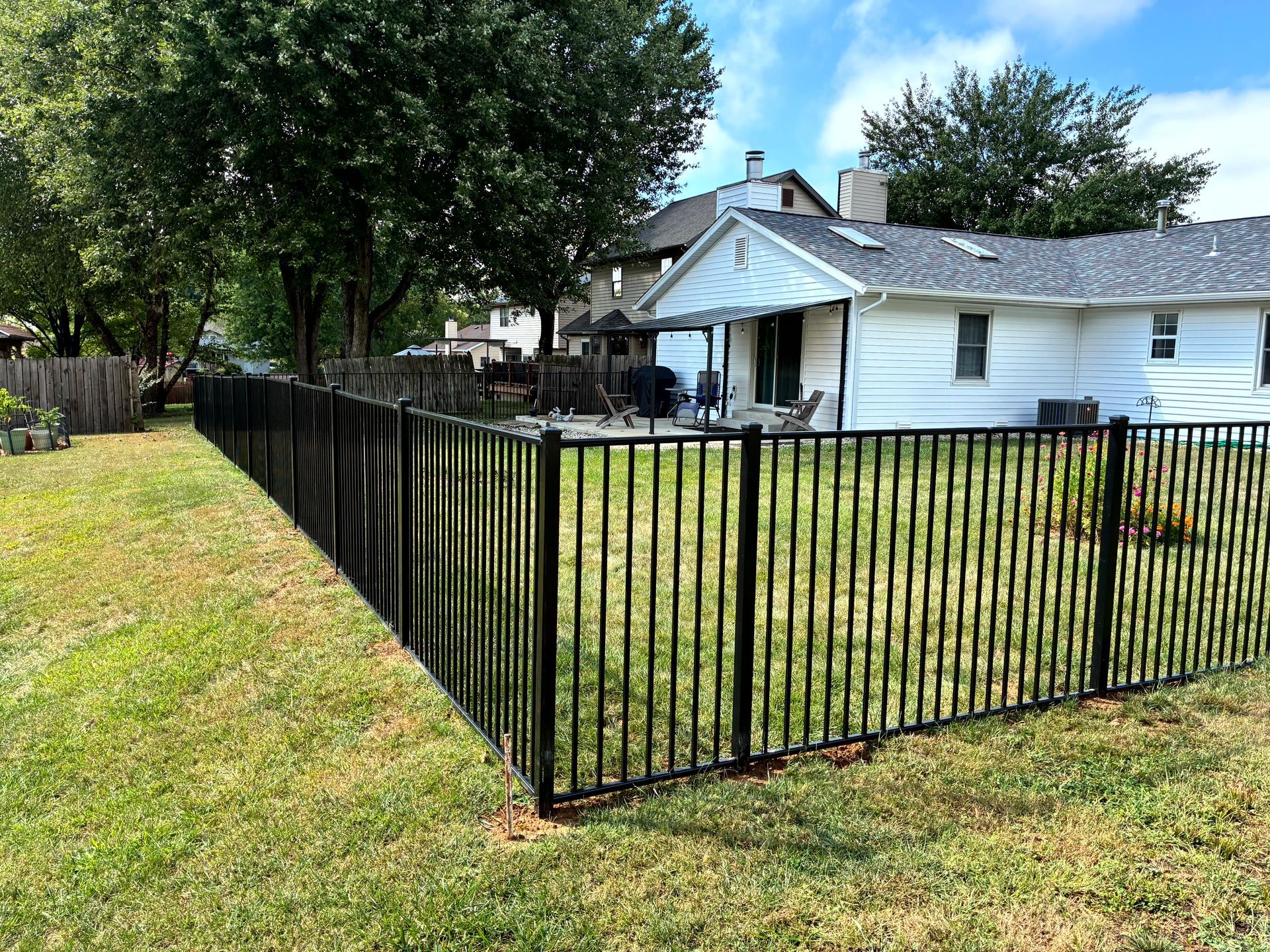 Black metal fence in a grassy yard, surrounding a white house with a patio.