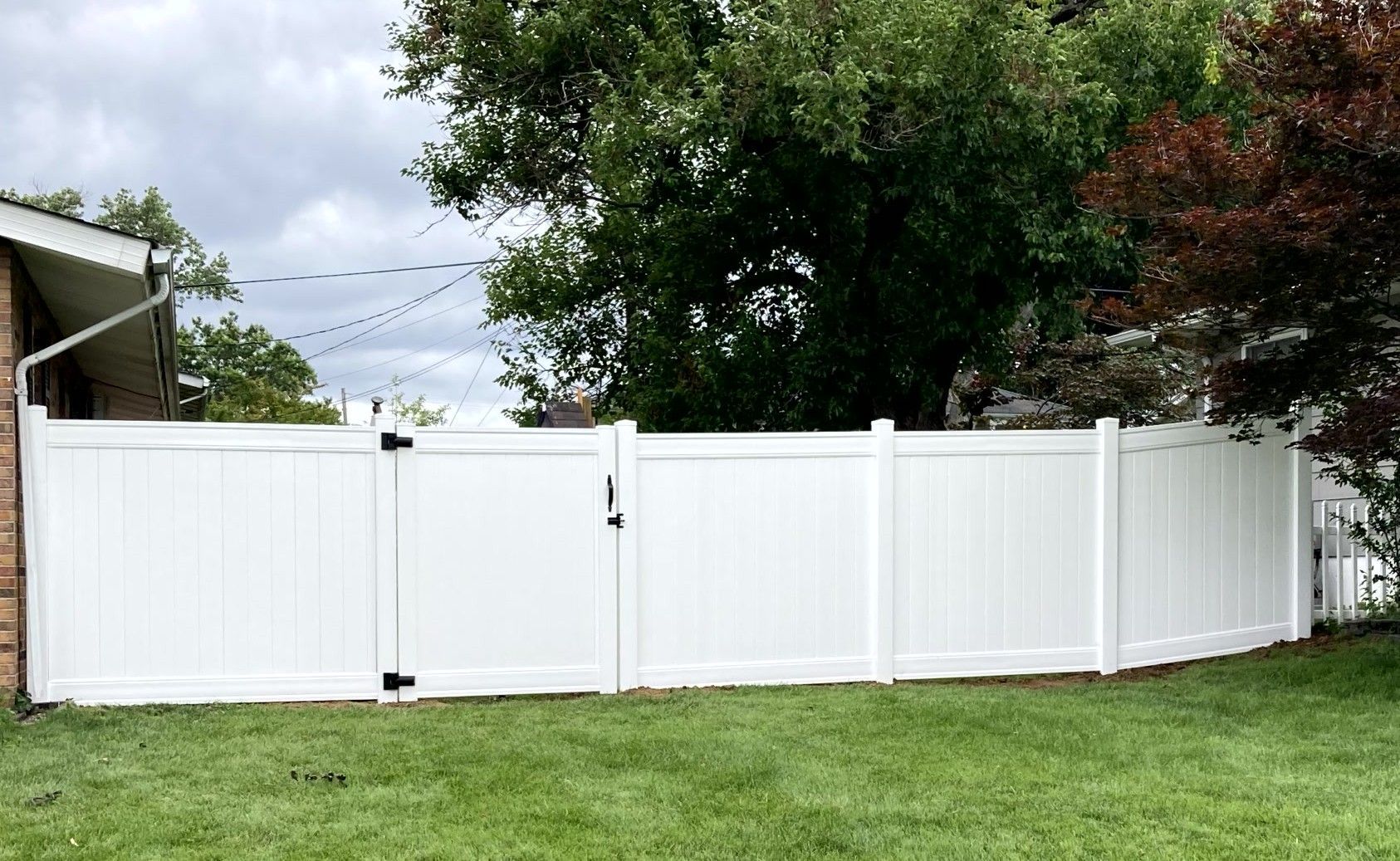 Black metal fence with small gate, green grass, and a building in the background.