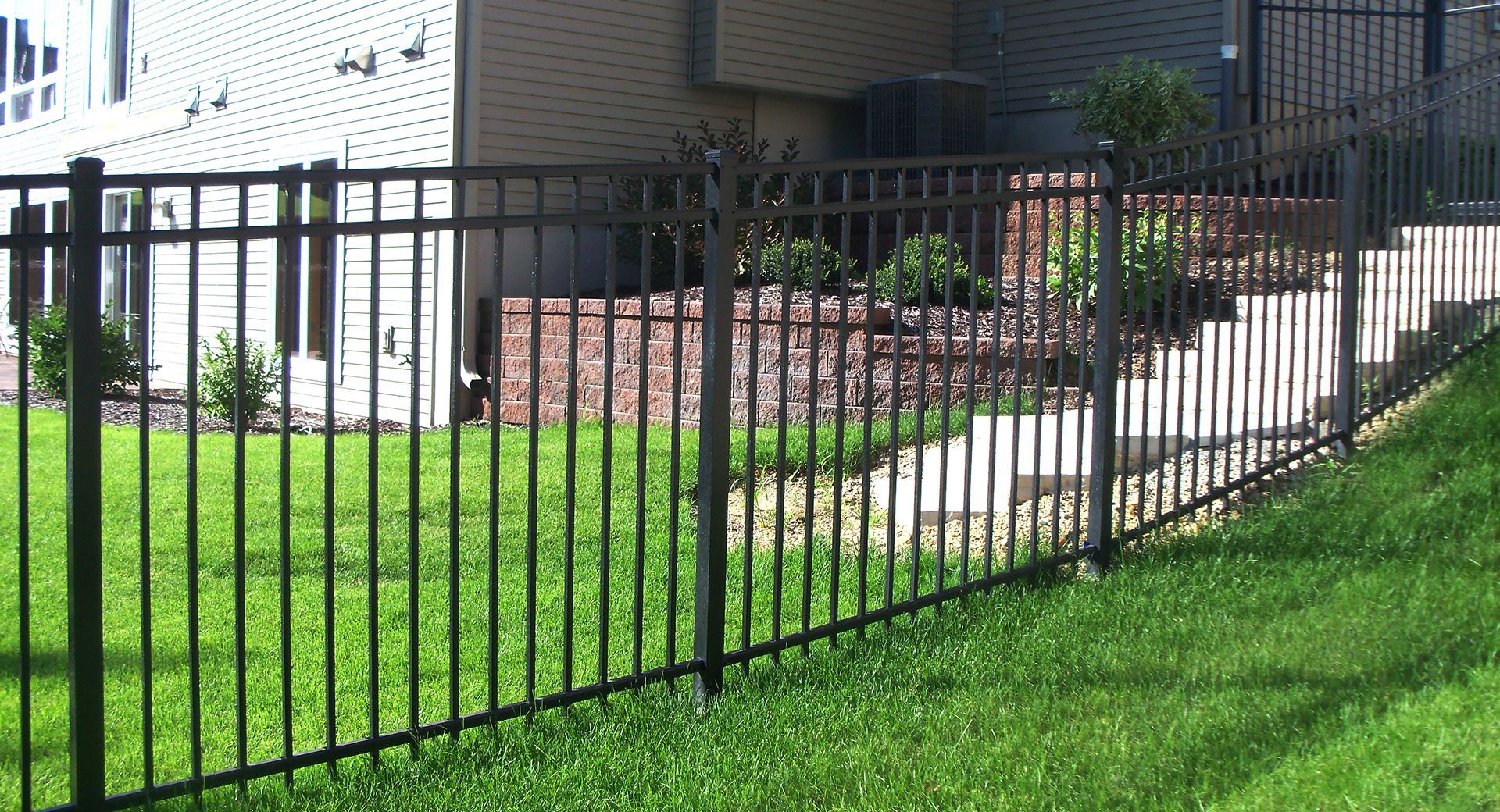 Black metal fence surrounding a yard with grass and building in the background.