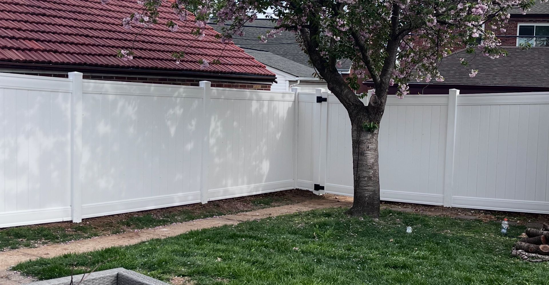 White vinyl fence in a backyard with a tree and green grass.