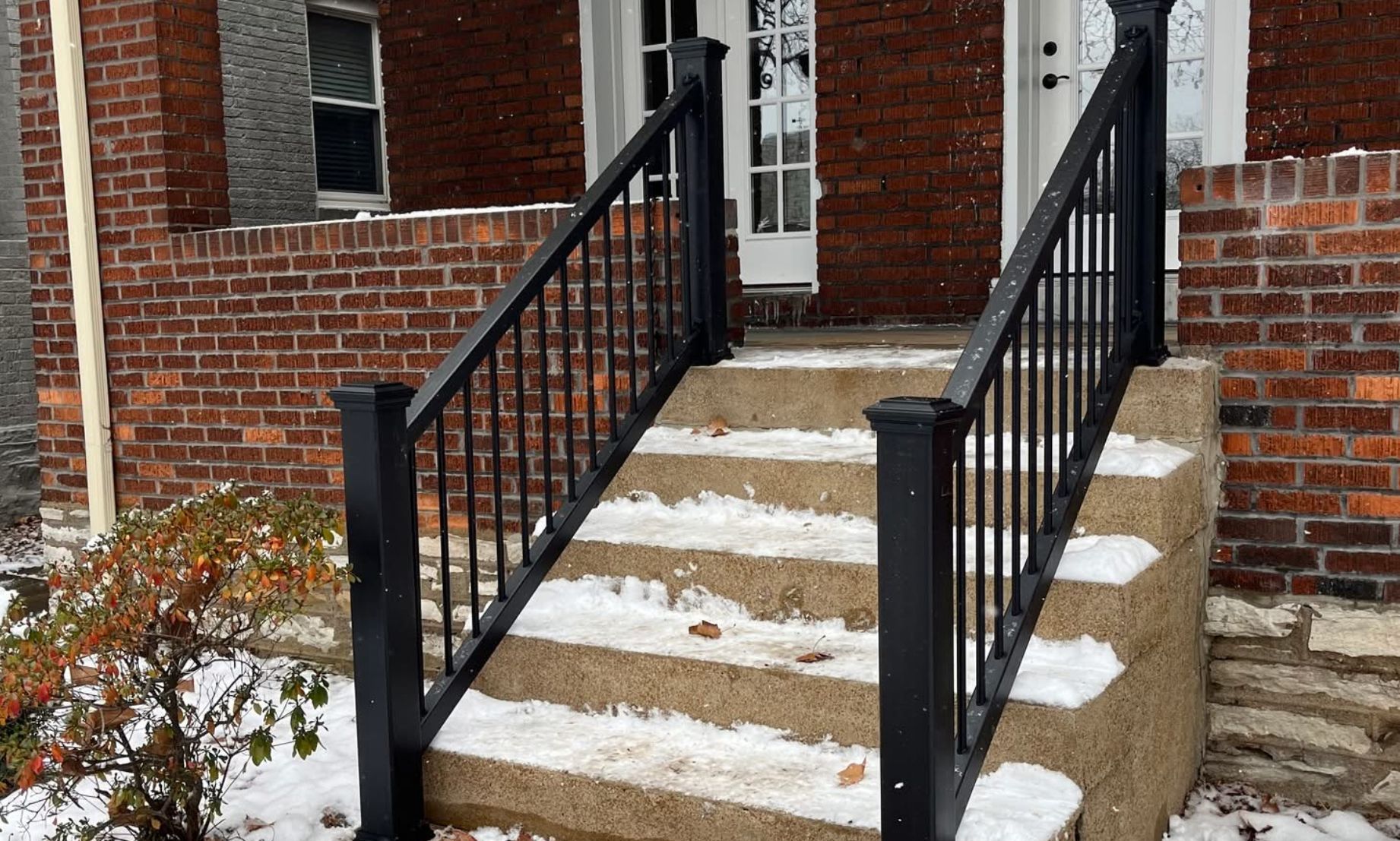 Brick building entrance with black railings and snow-covered steps.