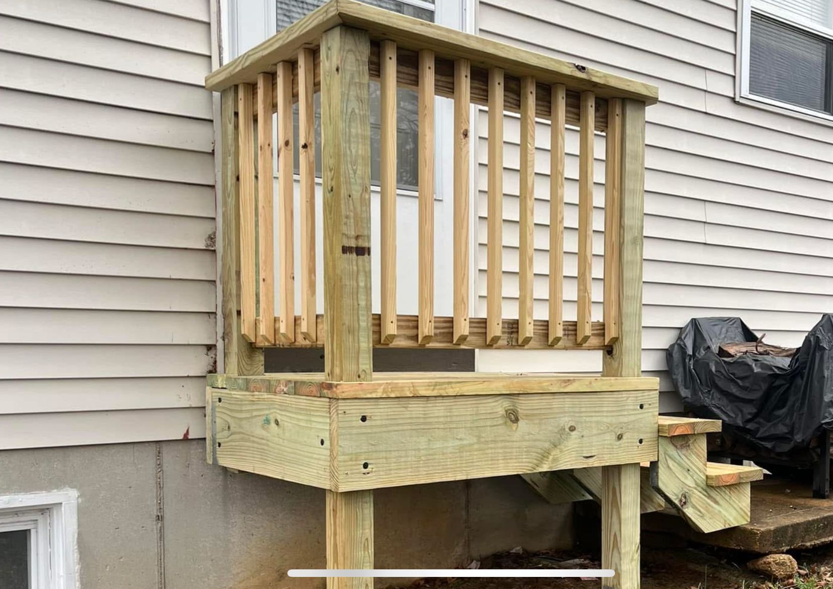 Wooden deck with railing attached to a beige house, with steps leading down.