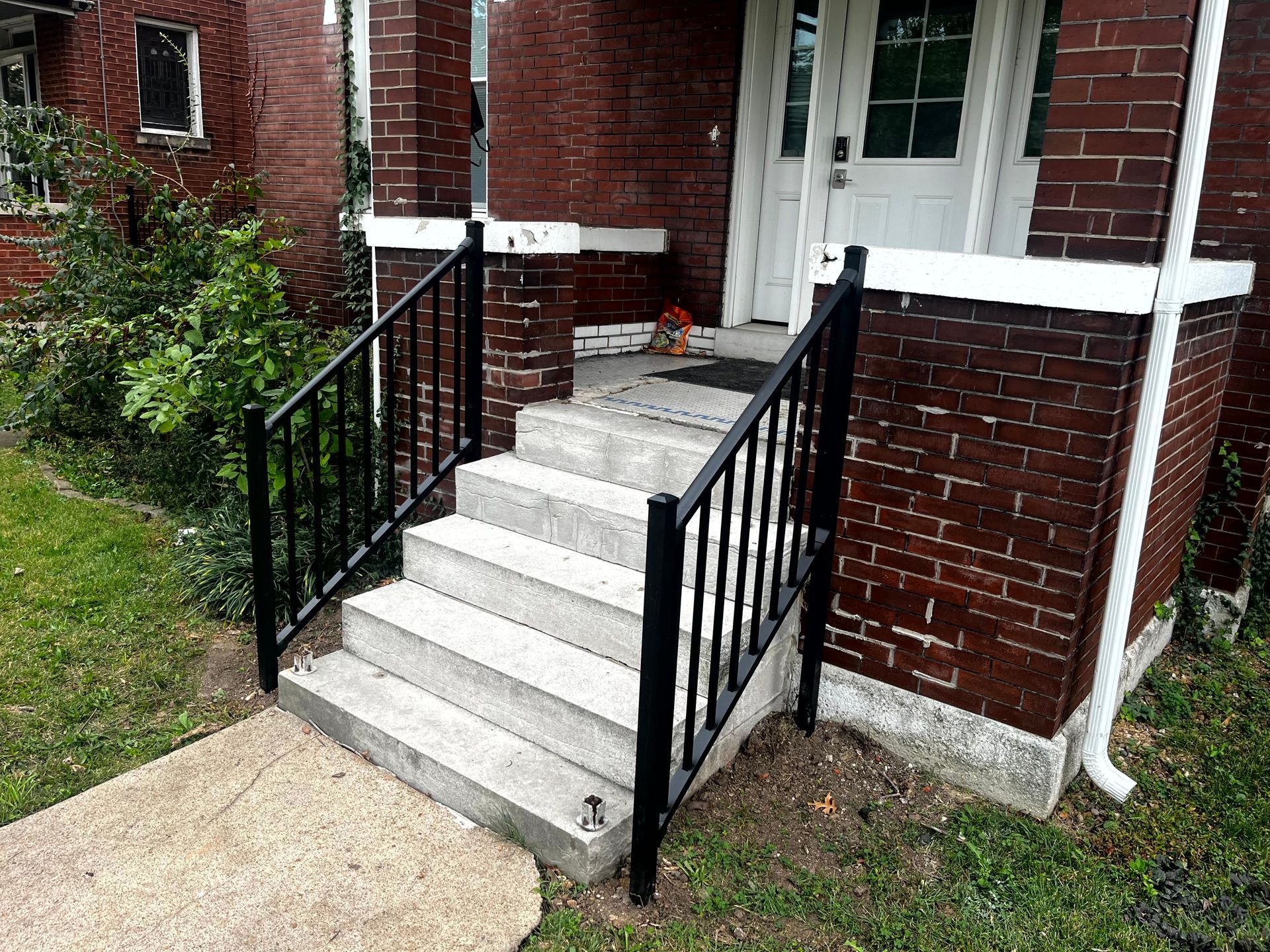 Exterior view of brick house with concrete steps and black handrails.