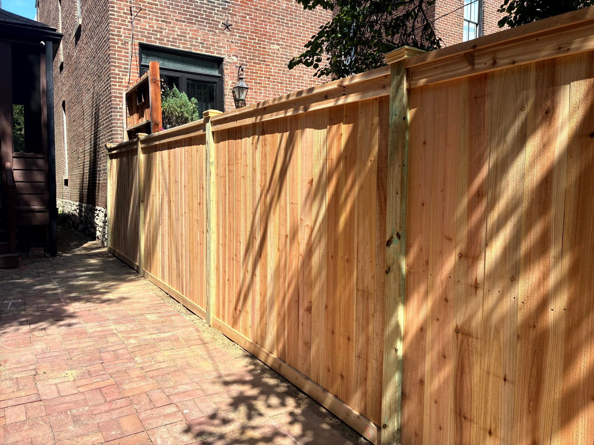 Wooden fence along a brick pathway next to a brick building.