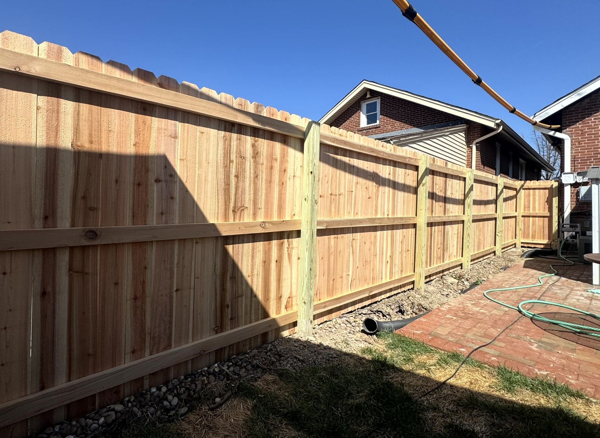 Deck with white pergola, black railing, supported by wooden posts on concrete blocks, set in a grassy yard.