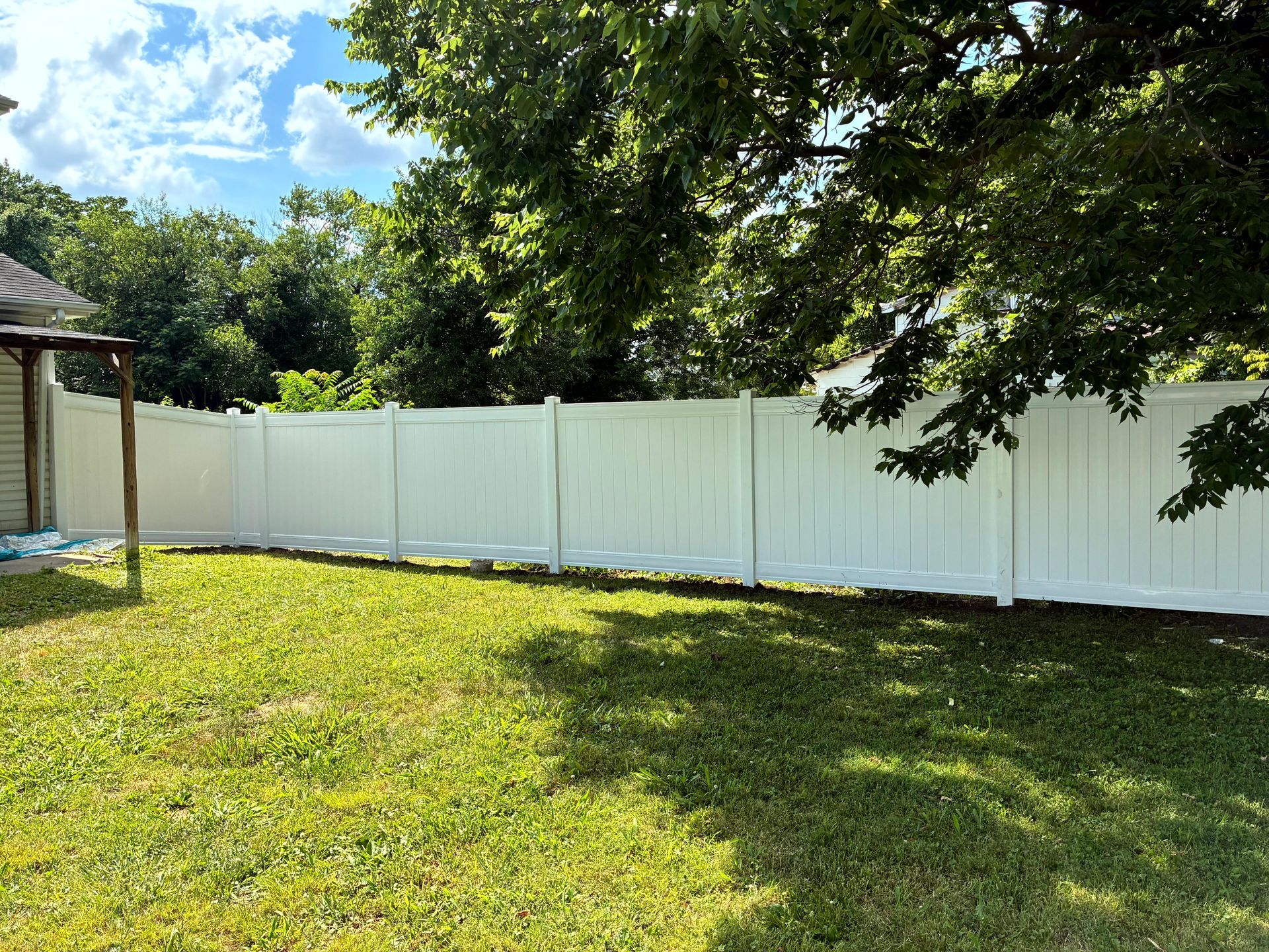 White vinyl fence in a grassy backyard, under a blue sky and tree shade.