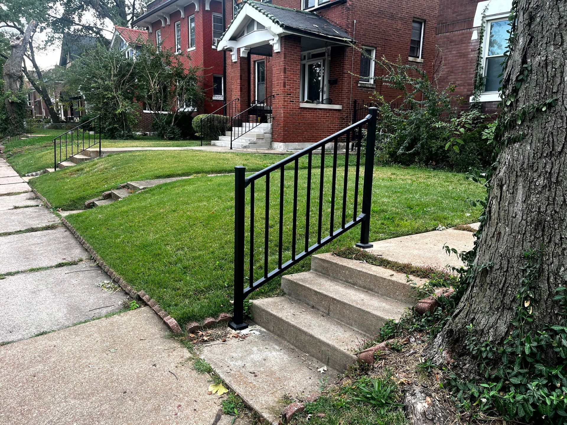 Black railing next to concrete steps leading up to a grassy yard and brick house.